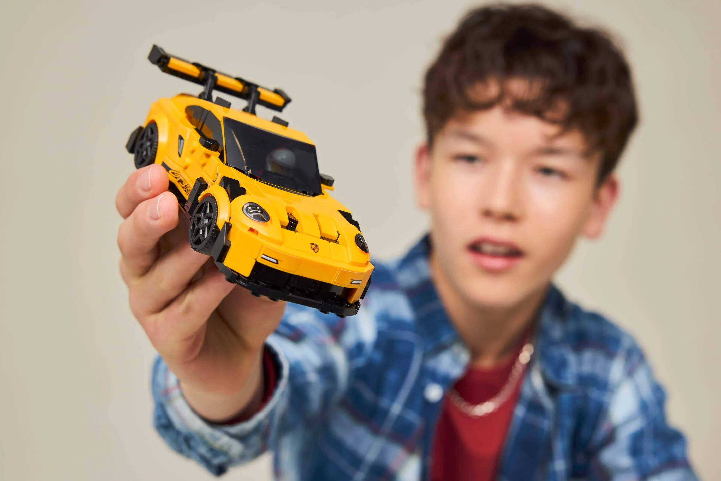 Un tânăr ține în mână modelul LEGO Porsche 911 GT3 RS, galben și detaliat.