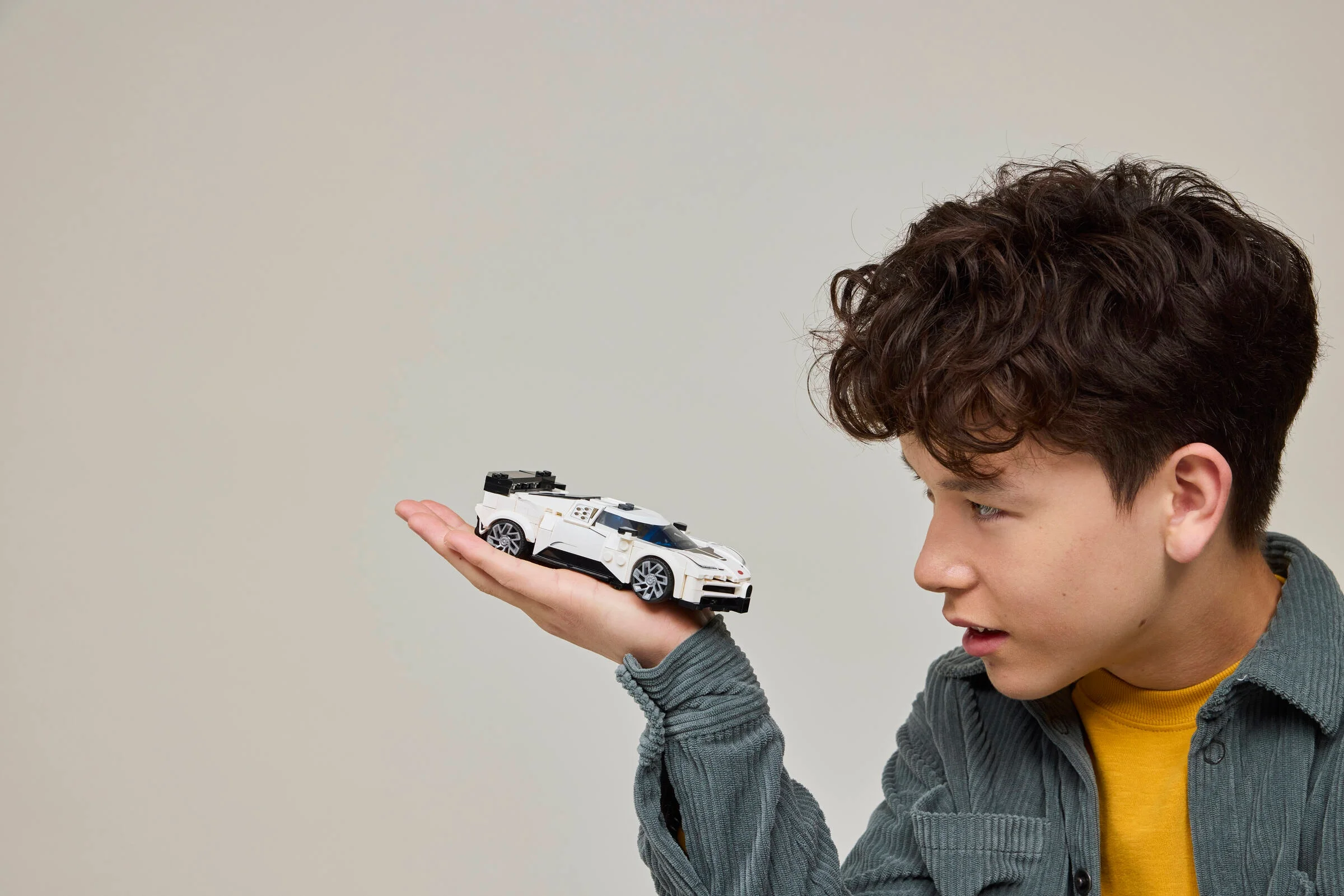 Un băiat admiră mașina Bugatti Centodieci LEGO, pe care o ține în palmă.