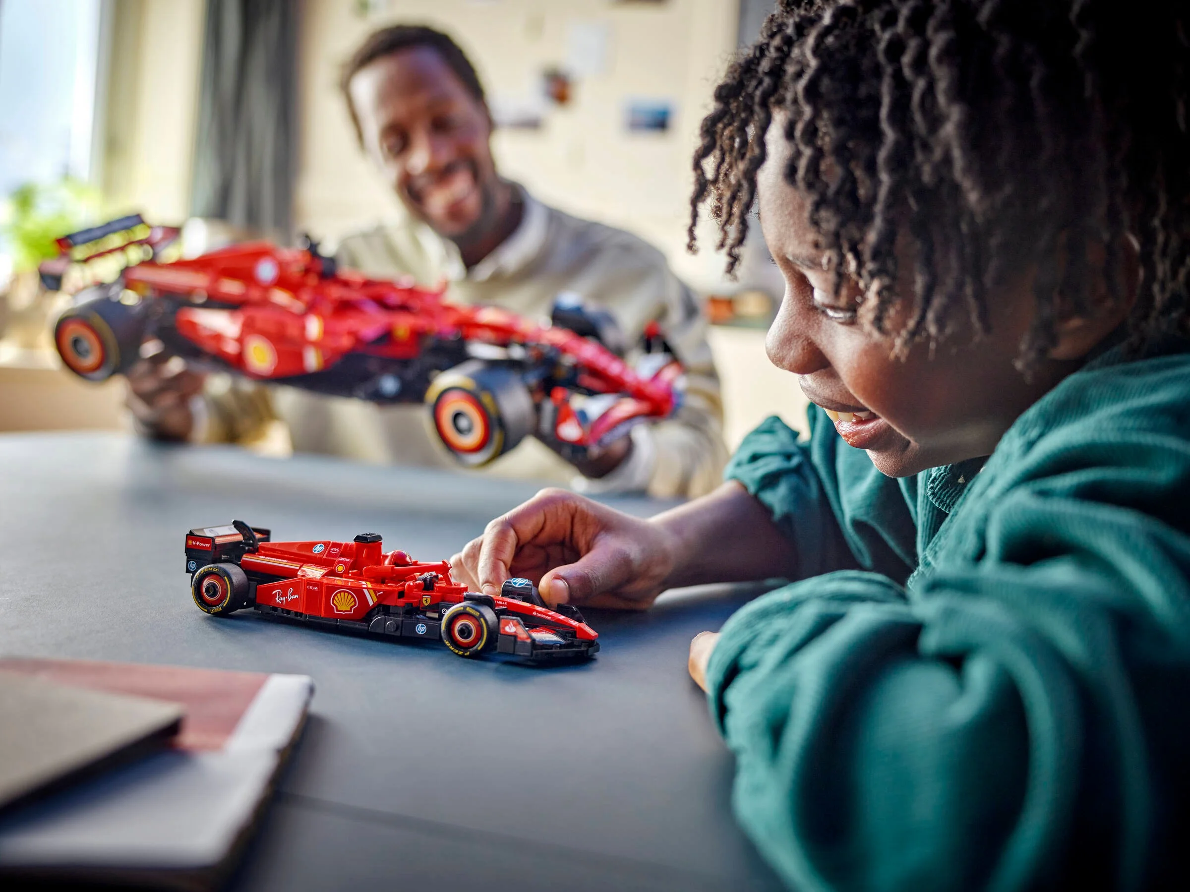 Un copil se joacă cu o mașină Ferrari SF-24 LEGO, în timp ce tatăl lui ține alta.