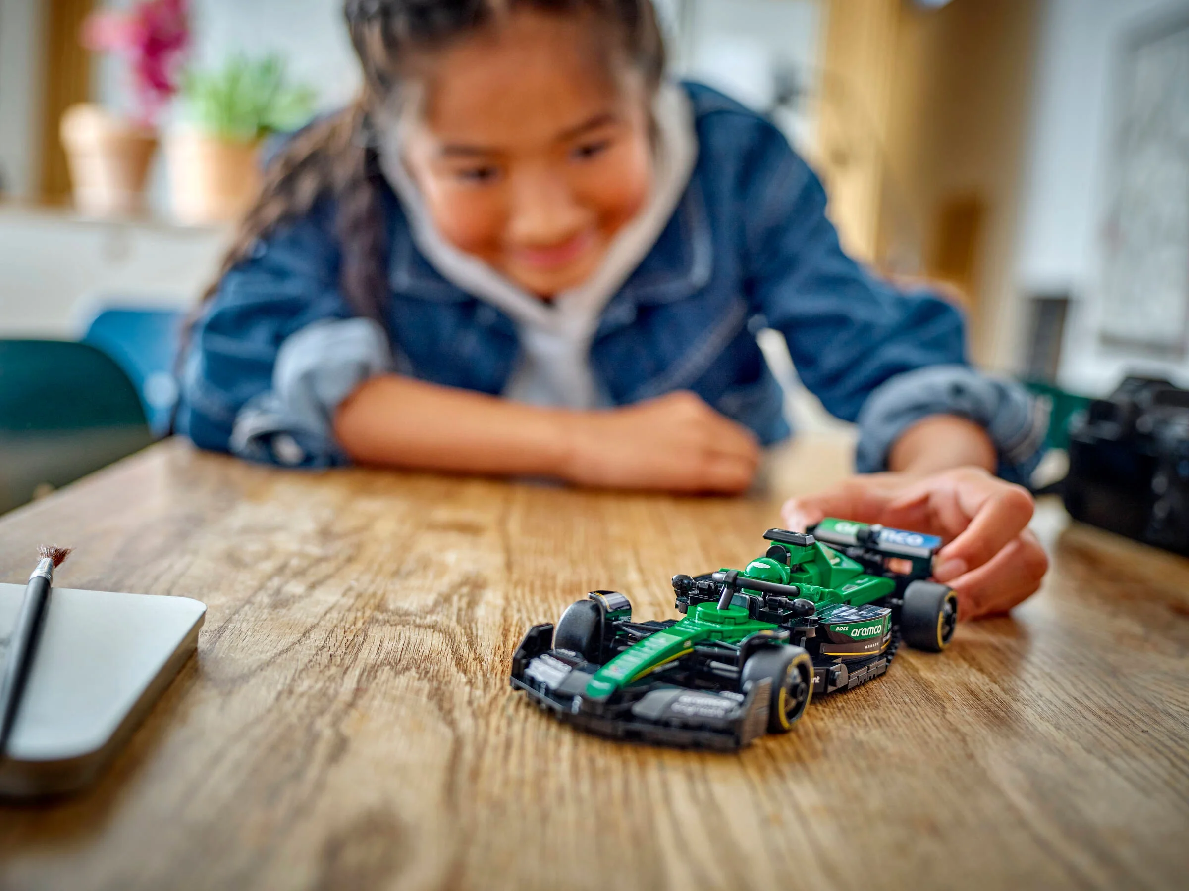 O fetiță se joacă cu modelul LEGO Aston Martin Aramco F1 AMR24 pe o masă de lemn.