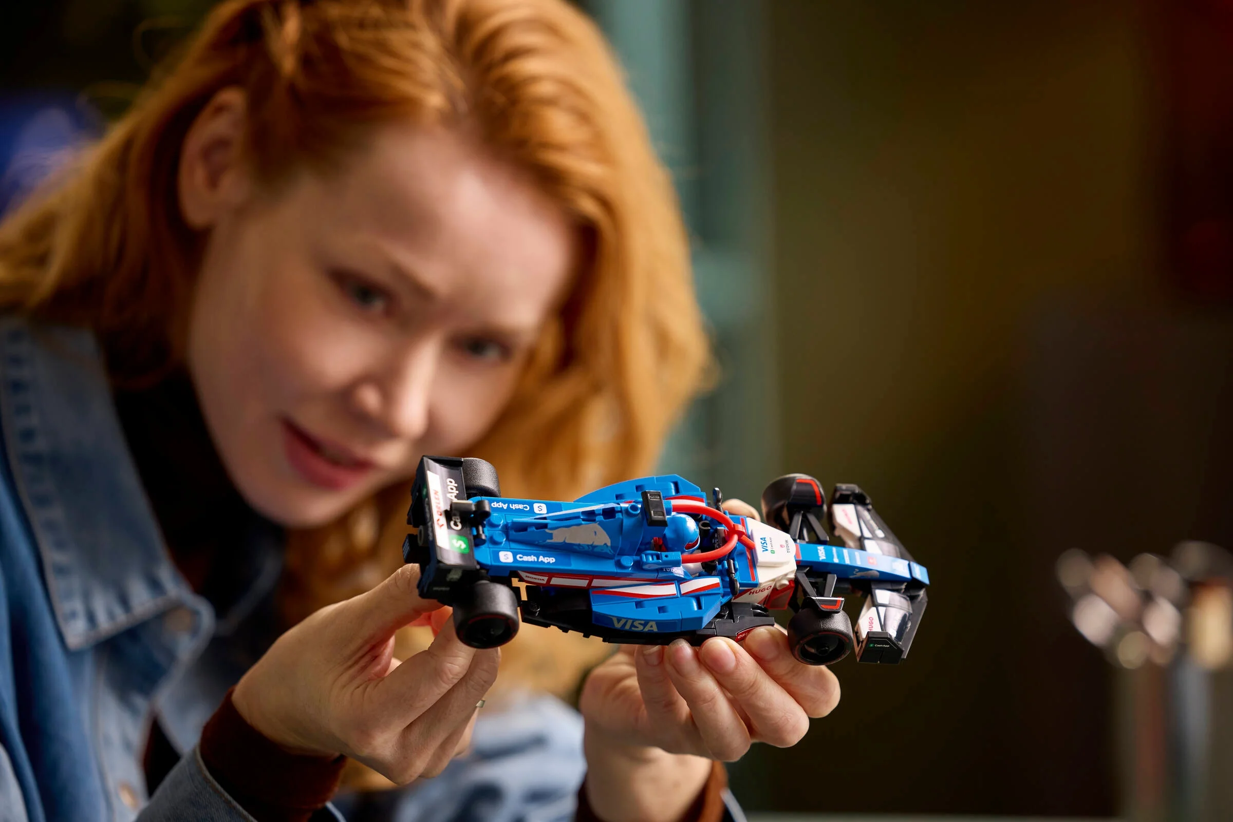 Femeie examinând modelul LEGO VCARB 01, evidențiind detaliile sponsorilor și designul mașinii.