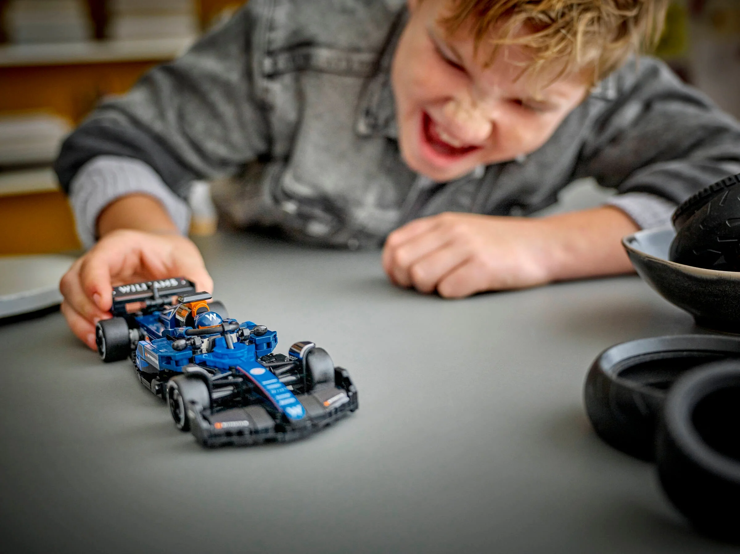 Un copil entuziasmat se joacă cu mașina Williams Racing FW46 LEGO. Bucurie pură!