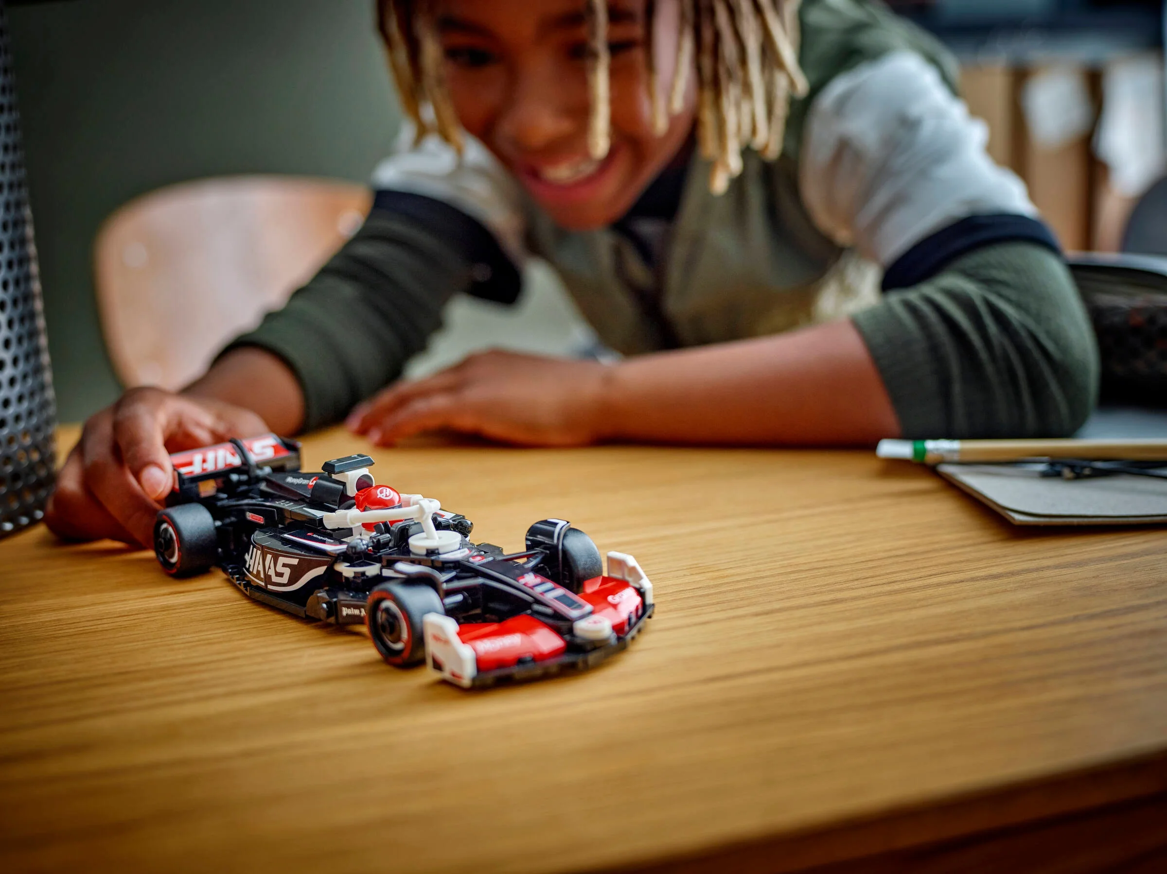 Un copil zâmbitor se joacă cu modelul LEGO Haas F1, pe o masă din lemn.