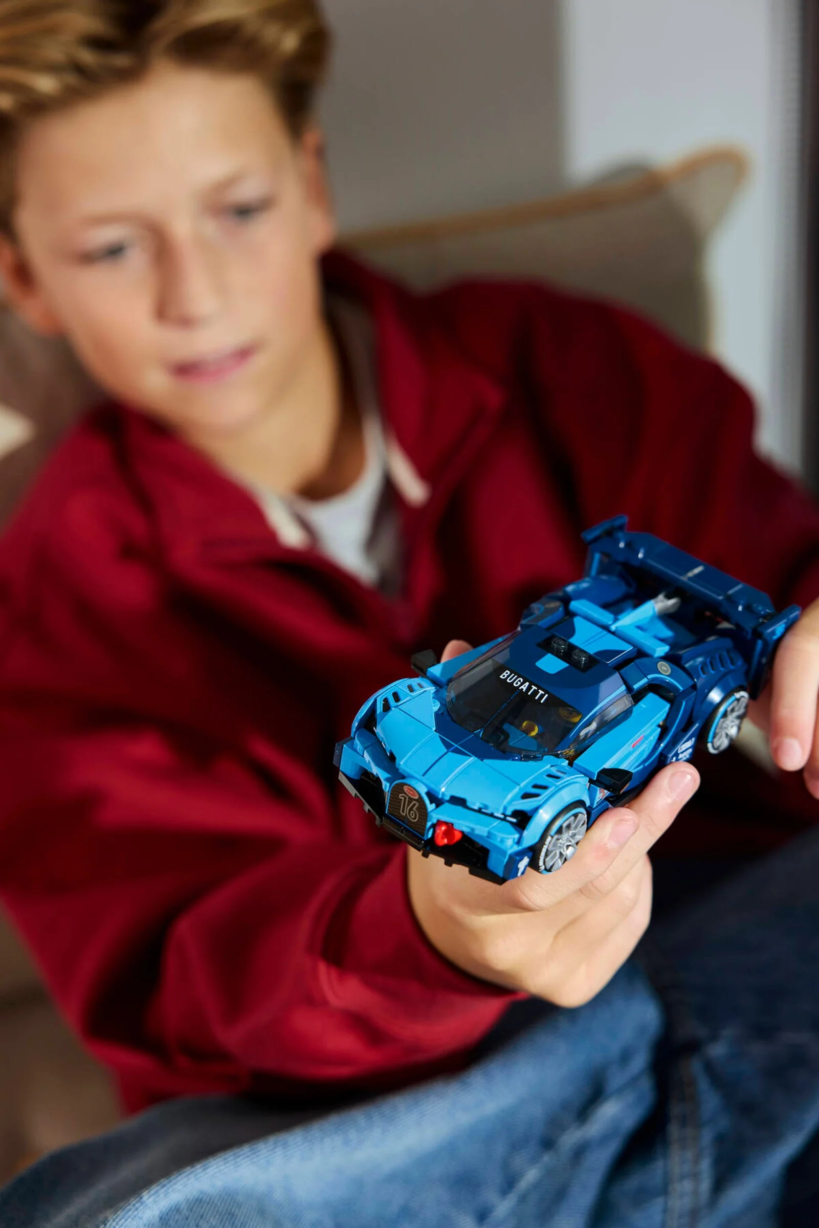 Băiat ținând în mână modelul LEGO Bugatti Vision Gran Turismo. Produsul este focalizat.