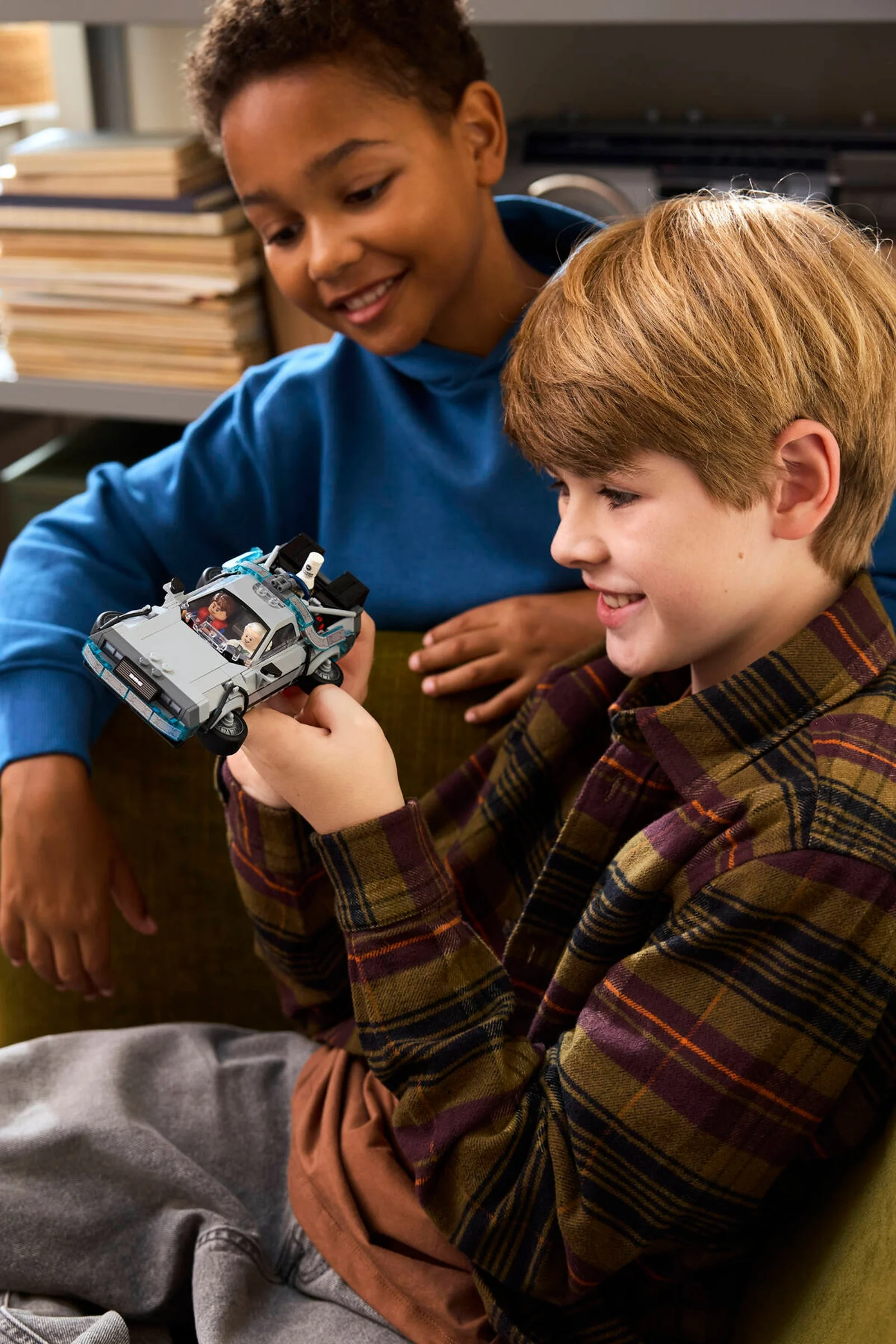 Doi băieți se joacă cu mașina timpului DeLorean LEGO. Zâmbete și bucurie pe fețele lor.