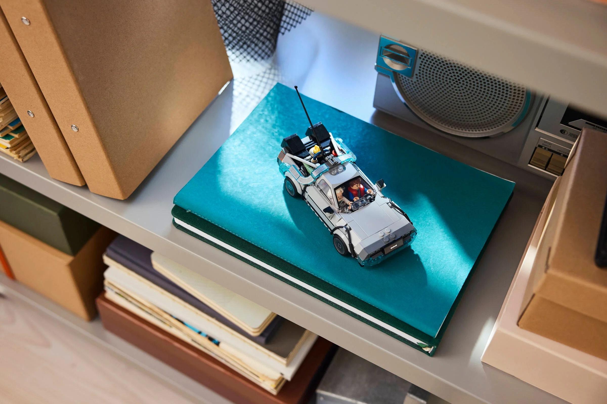 Mașina timpului DeLorean LEGO, un model detaliat expus pe o poliță, alături de alte obiecte.