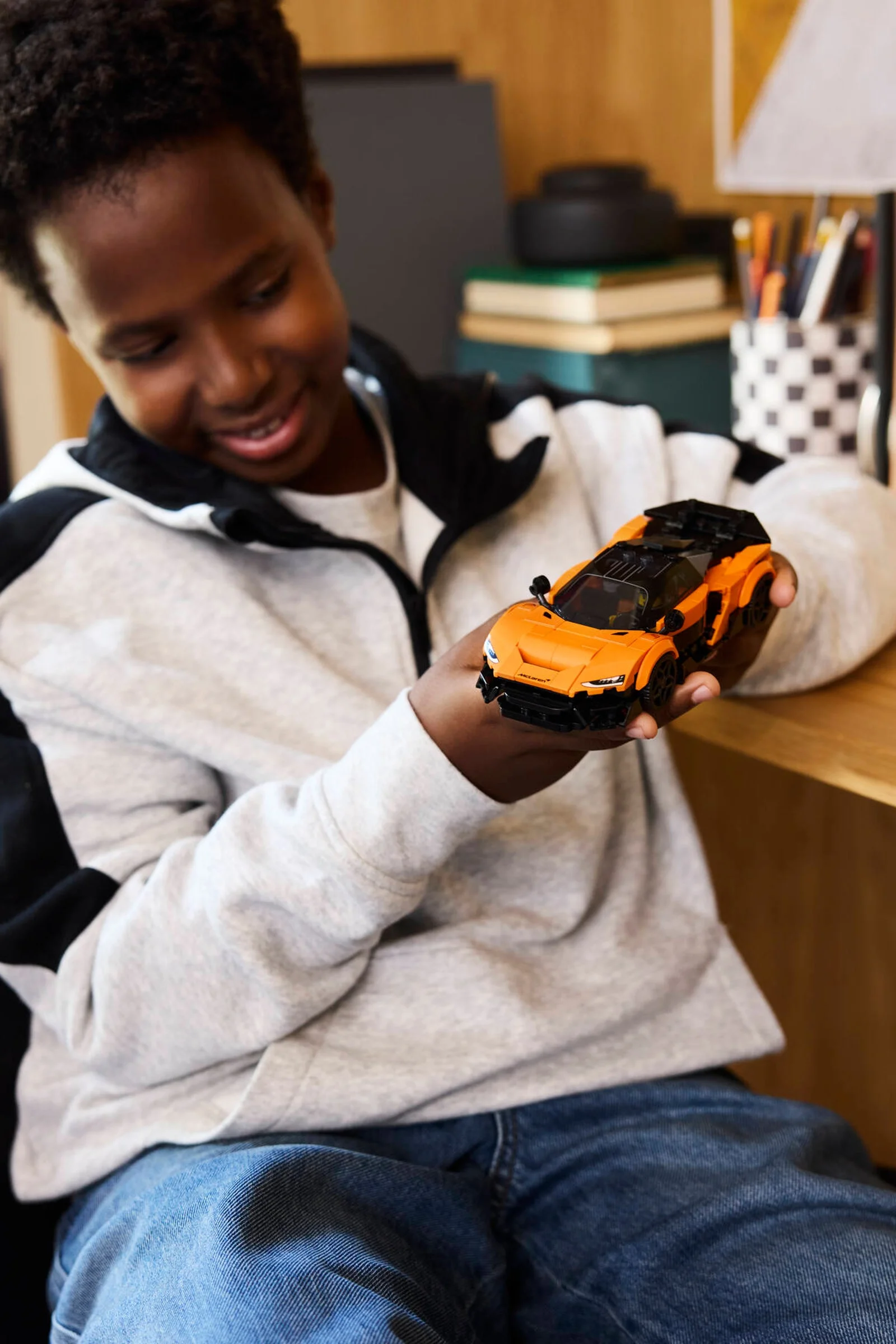 Băiat zâmbitor ținând McLaren Solus GT portocaliu, construit din LEGO.