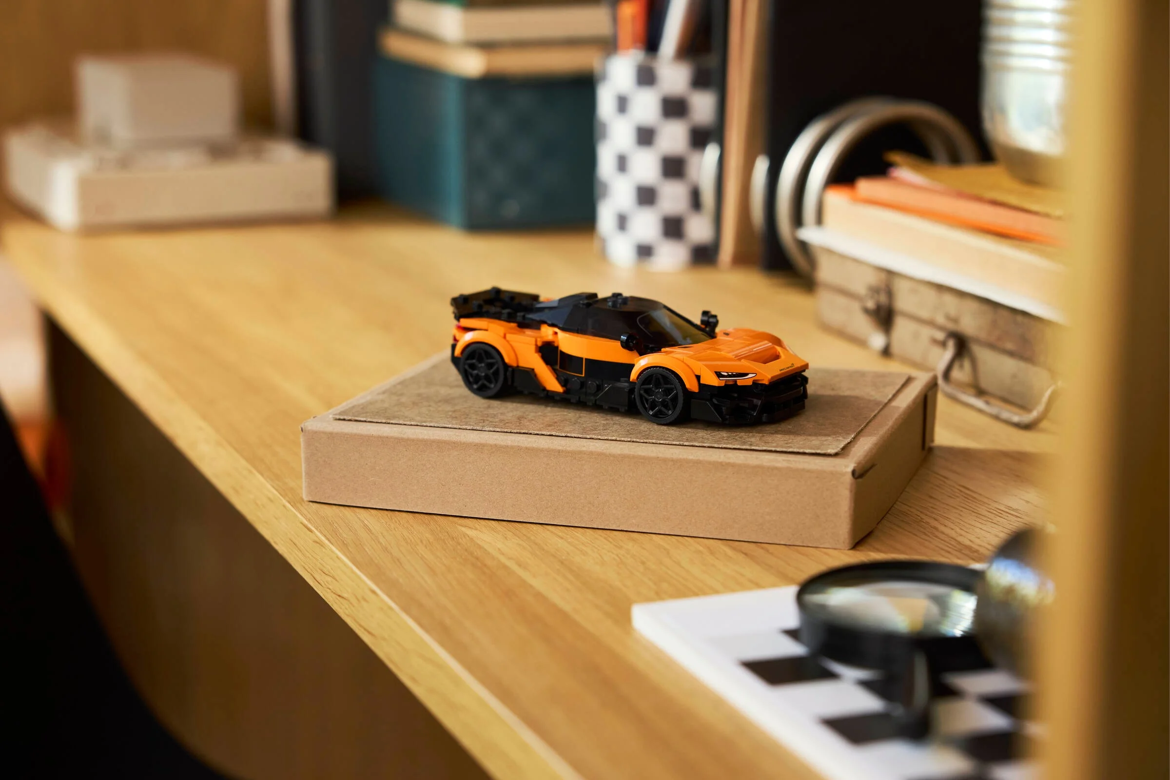 Modelul LEGO McLaren W1 portocaliu-negru pe o cutie, într-un decor ambiental.
