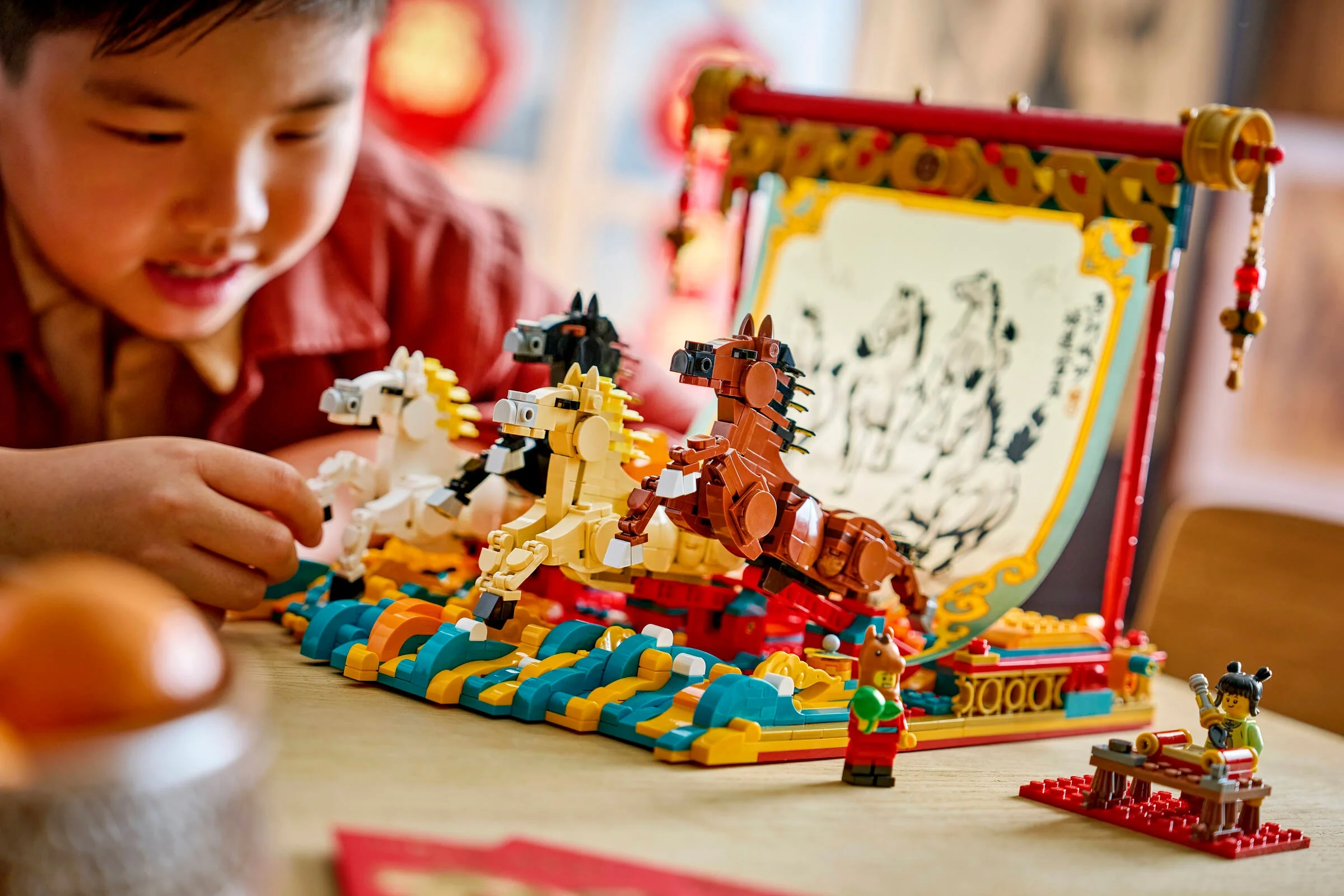 Copil construind setul LEGO 80119 cu cai galopanți și un tablou tradițional chinezesc.