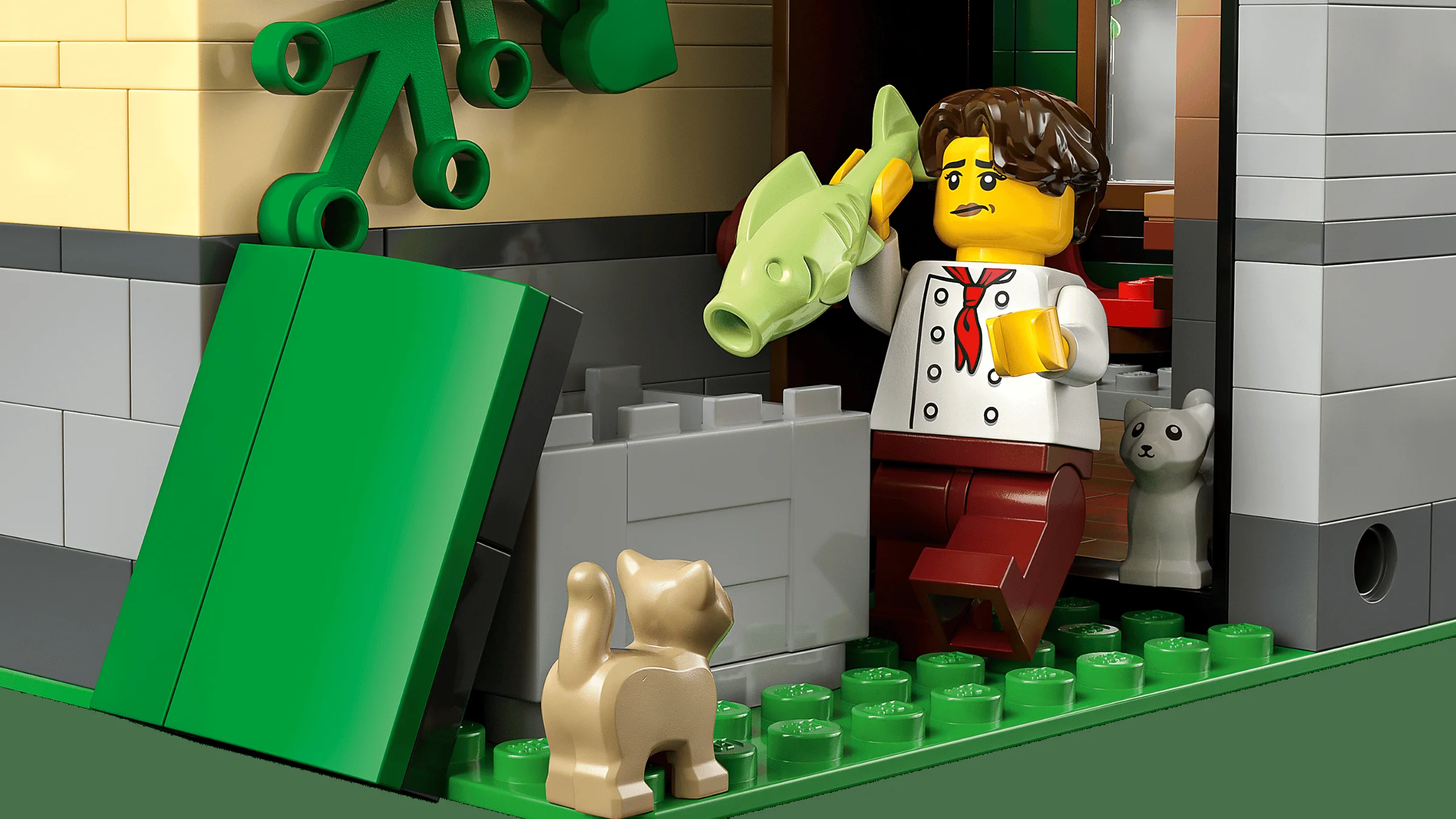 Prim-plan cu un bucătar ce ține un pește, alături de două pisici LEGO.