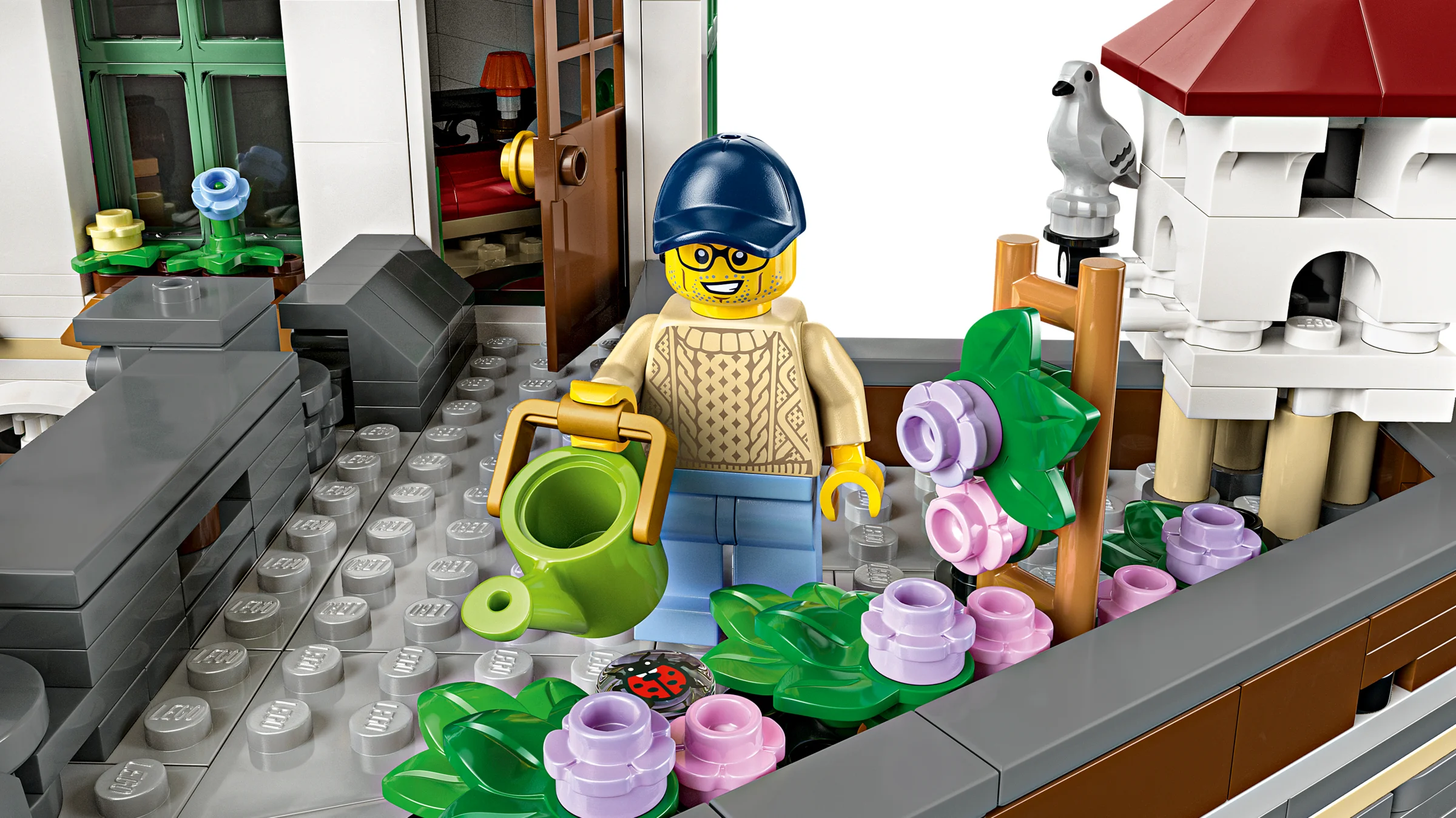Minifigurina udă florile pe acoperișul clădirii. Detaliu al setului LEGO Shopping Street.