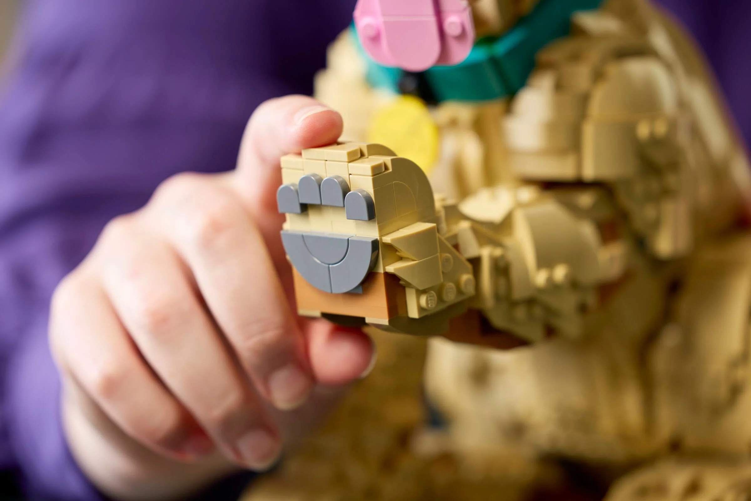 O mână ține lăbuța detaliată a cățelușului Golden Retriever LEGO. Detaliu de construcție.