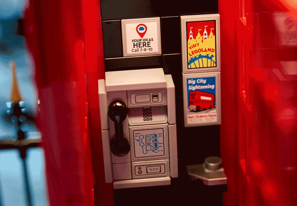 Detaliu cu telefonul public, reclame și afișe turistice în cabina telefonică roșie LEGO.