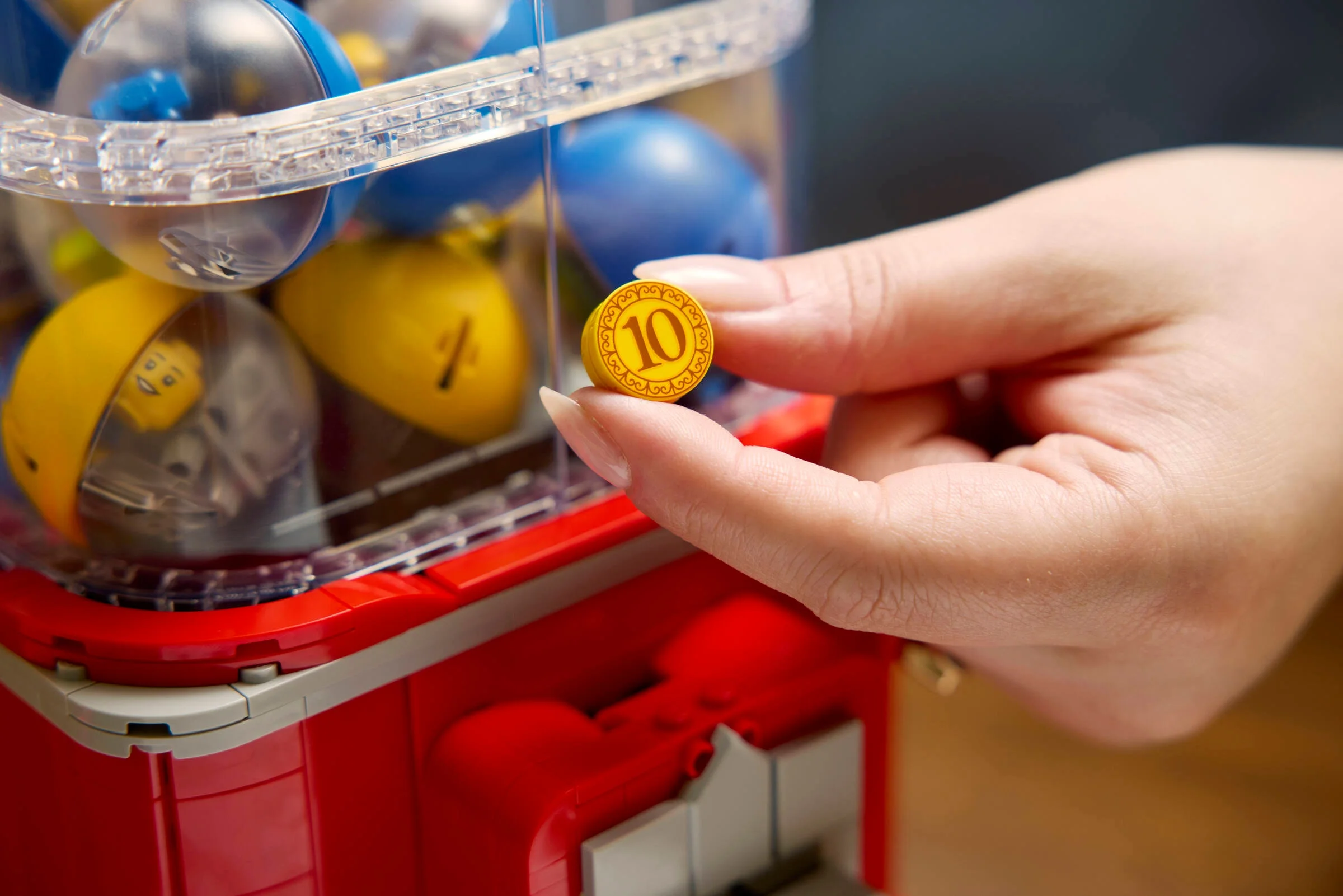 Monedă LEGO în mână, detaliu din setul 21358. Elemente transparente și capsule colorate vizibile.