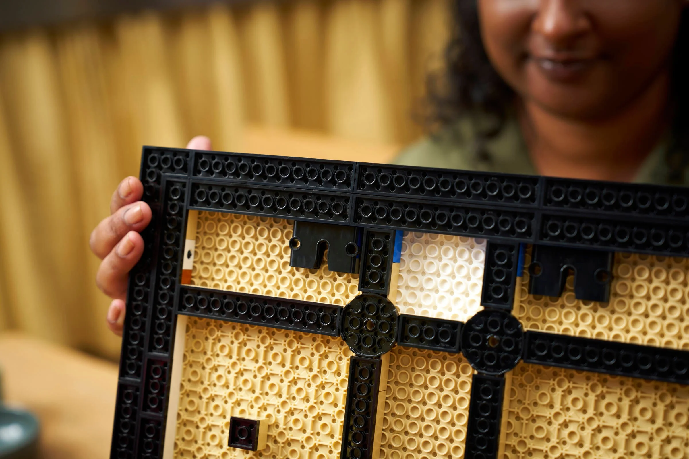 Construcția bazei modelului LEGO, cu piese bej și negre. O persoană ține baza în mână.