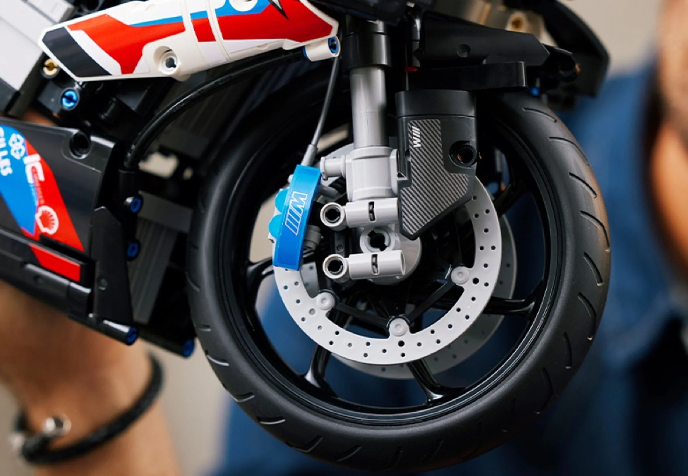 Detaliu prim-plan cu roata față a motocicletei BMW M 1000 RR LEGO Technic, etrier albastru.