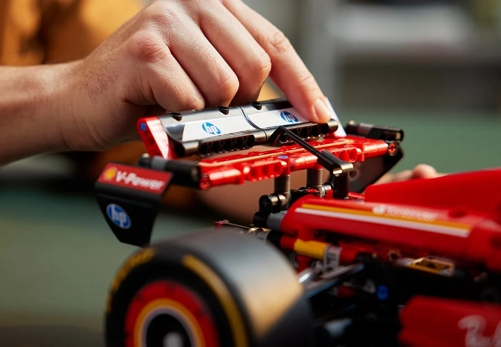 O persoană atașează un detaliu la modelul Ferrari SF-24 F1, accent pe sigle și construcție.