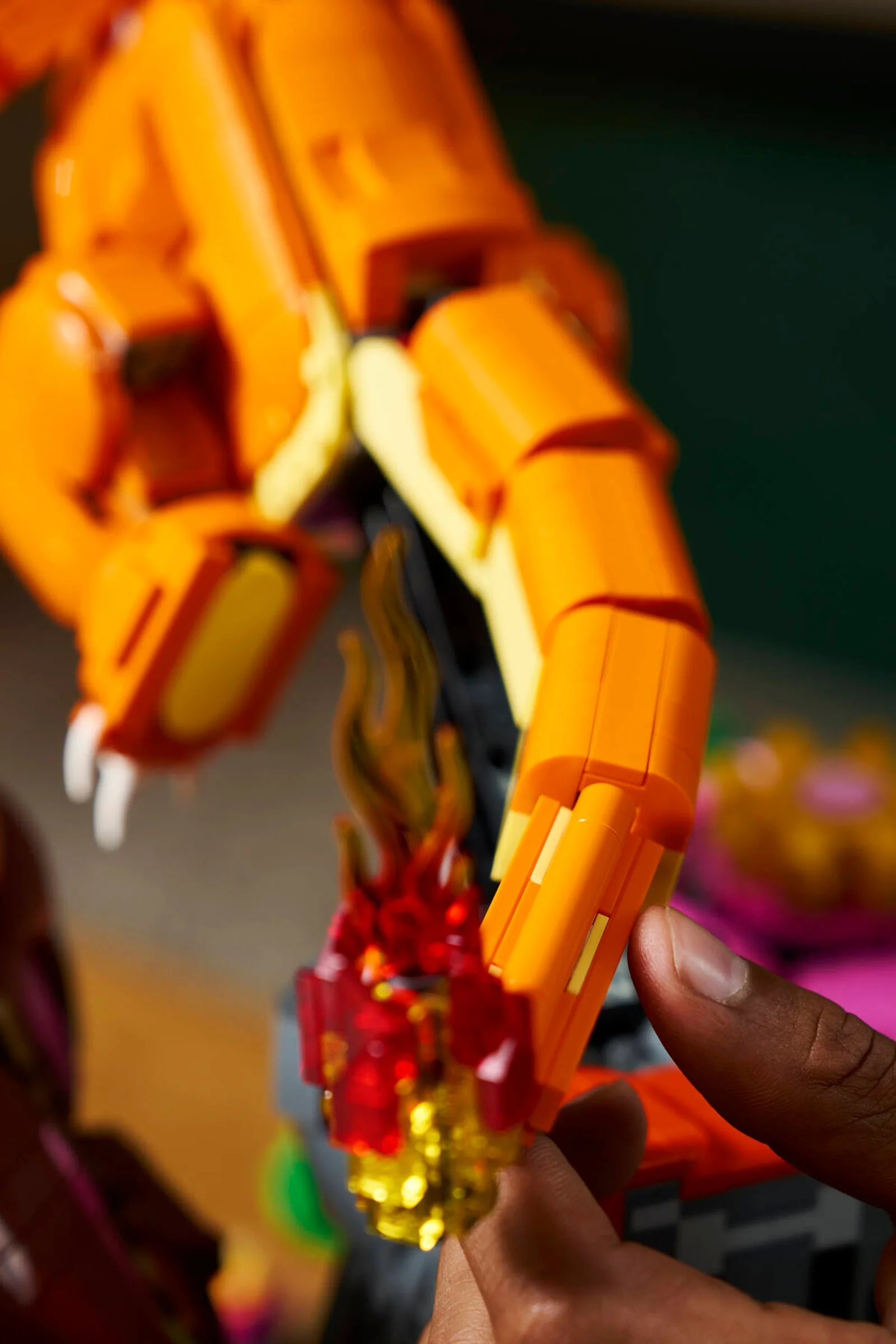 Prim plan cu Charizard LEGO. Văzut coada cu flăcări și cineva care interacționează cu modelul.