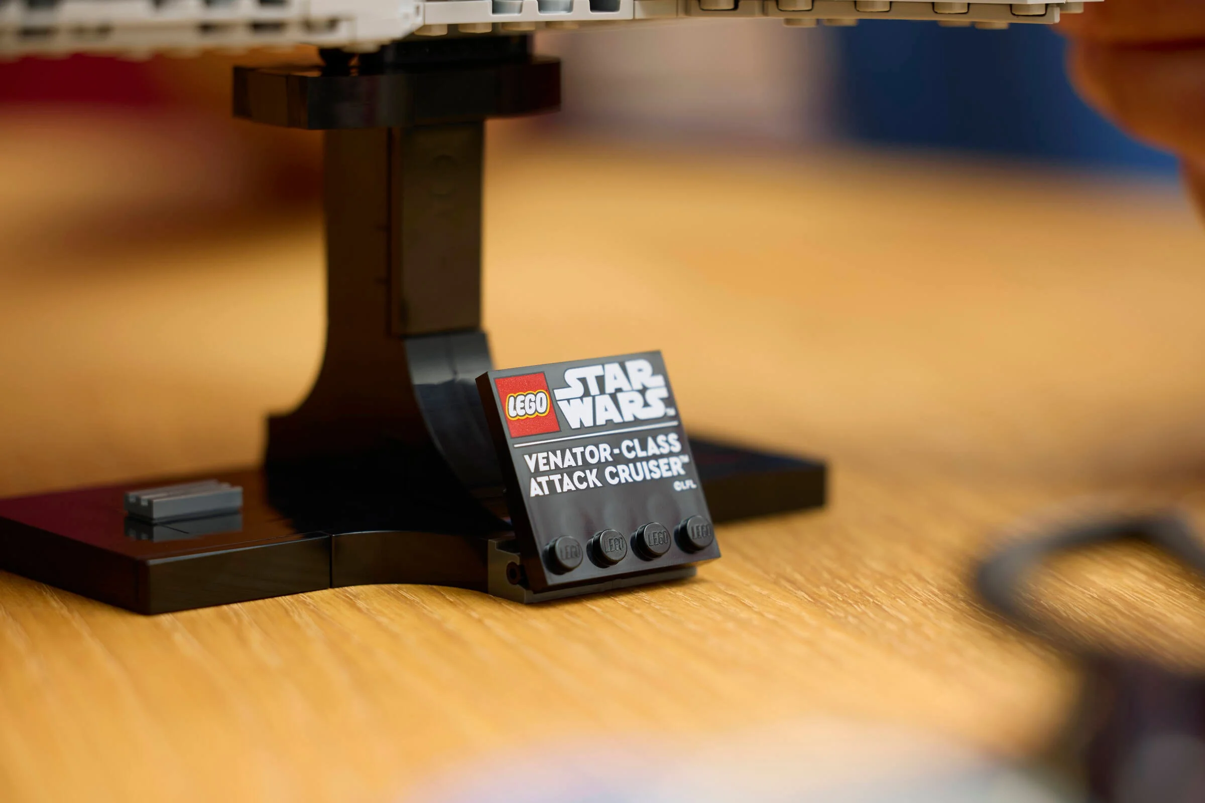 Prim-plan cu plăcuța LEGO Star Wars Venator-Class Attack Cruiser, cu suportul modelului în spate.