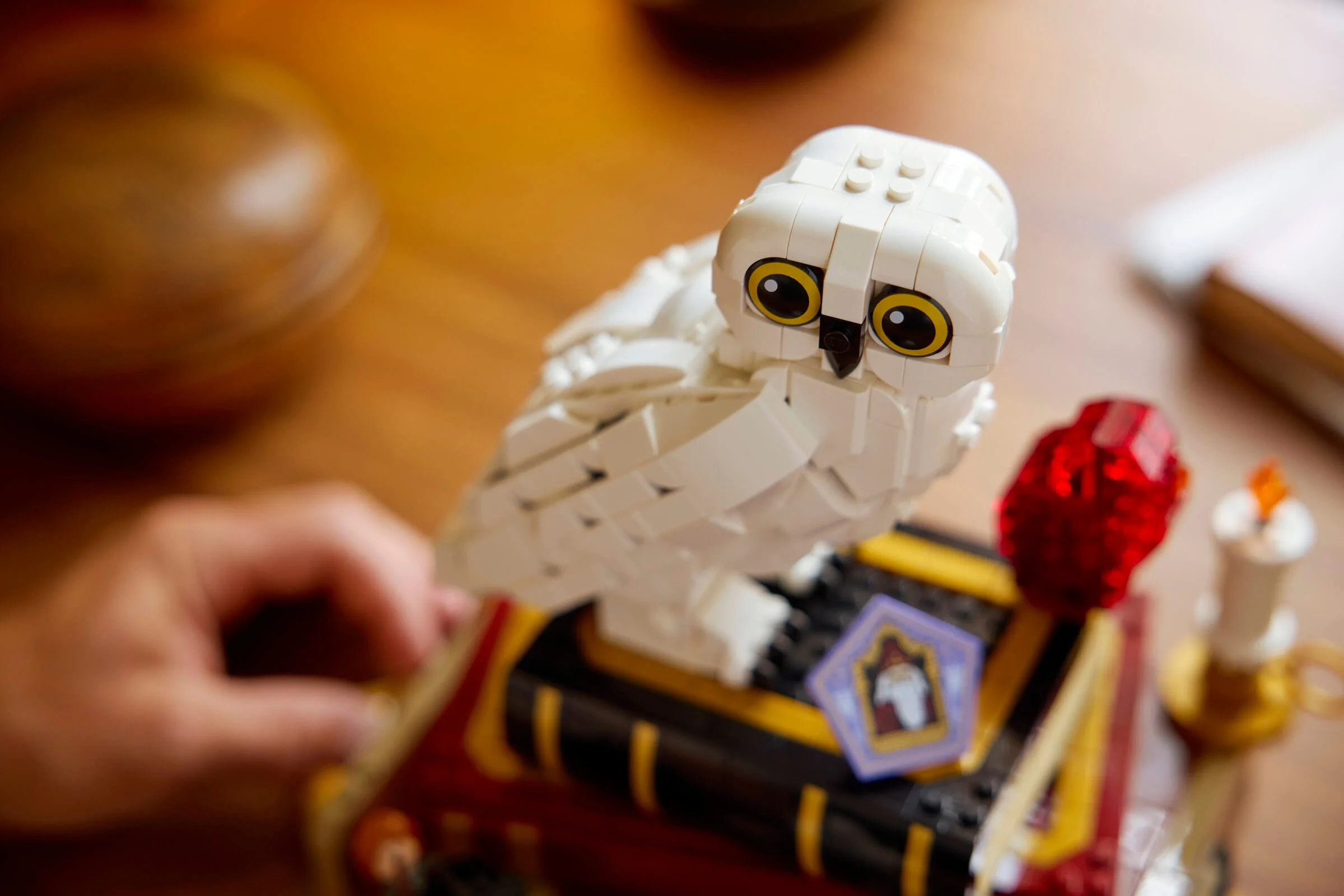 Prim-plan cu bufnița Hedwig LEGO, pe un set cu cărți și piatra filosofală roșie.