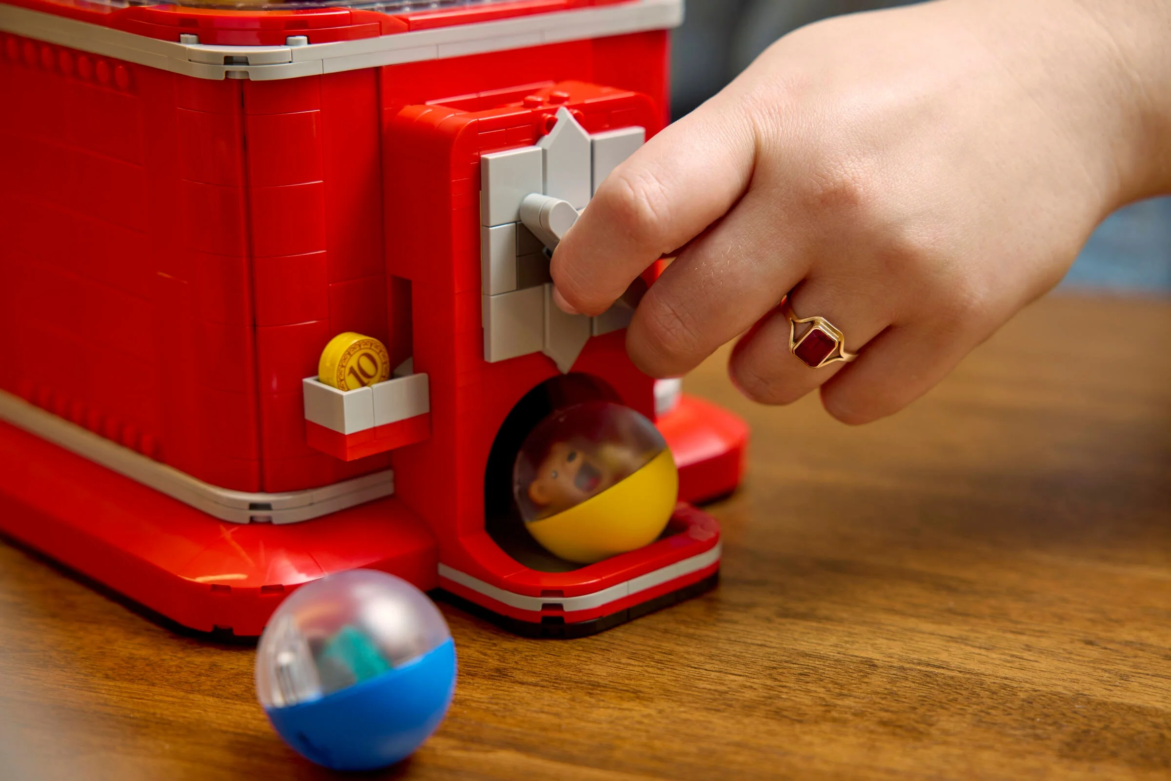 Mașină de vending minifigurine. Mâna rotește manivela, o capsulă cu minifigurină cade afară.