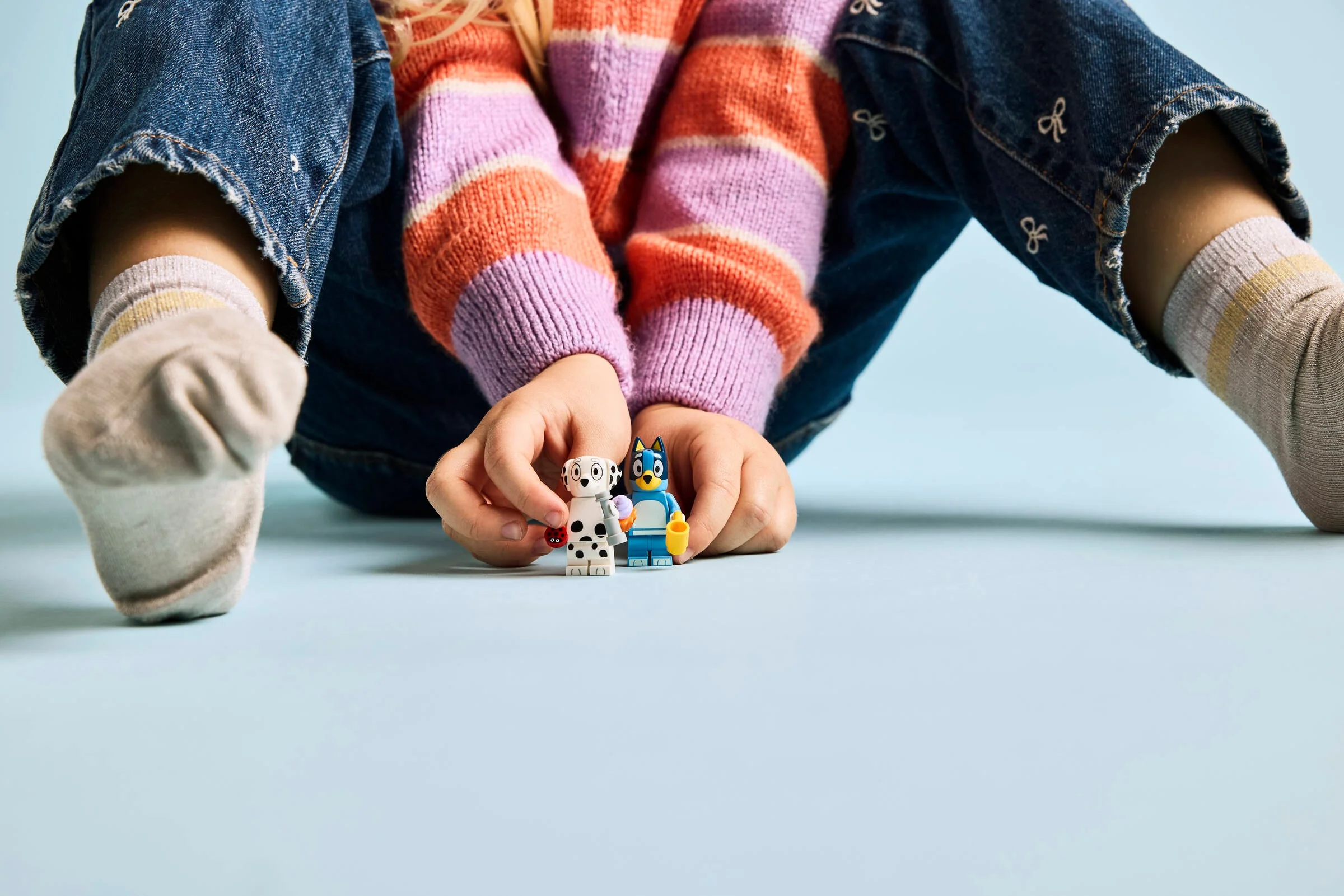 Un copil ține minifigurinele Bluey și Chloe, evidențiind interacțiunea umană.