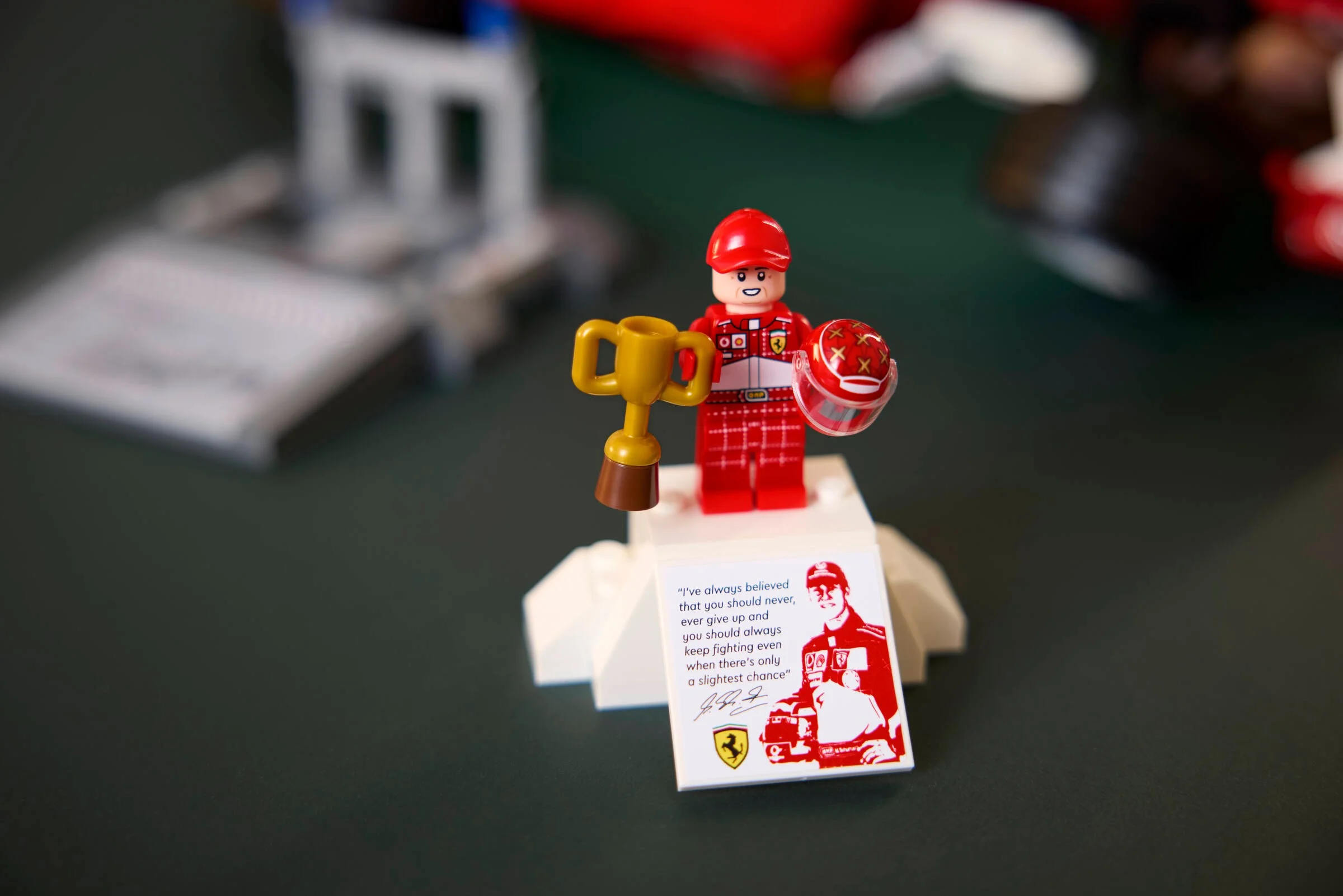 Prim-plan cu minifigurina Michael Schumacher, trofeu și citat inspirațional.