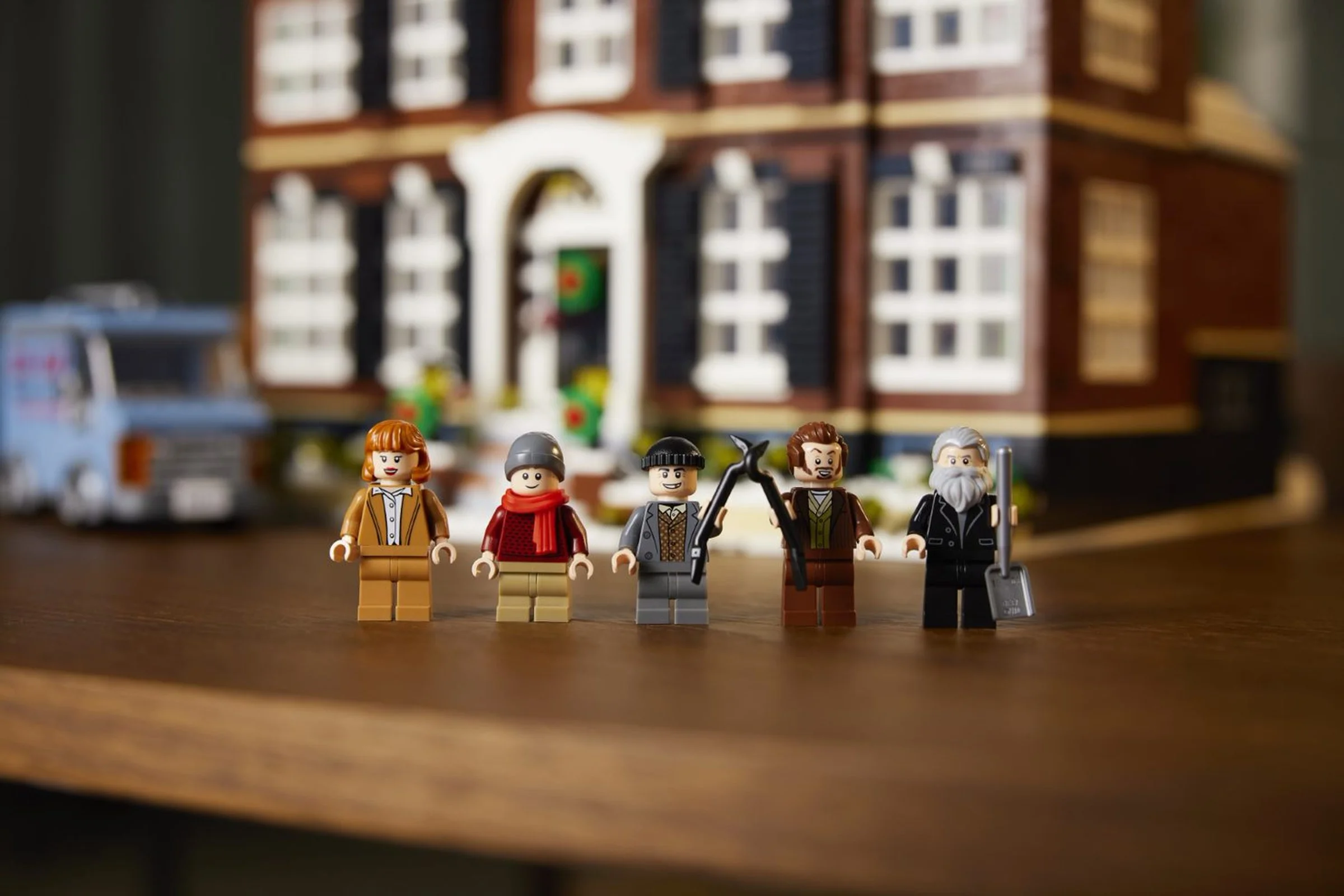 Minifigurinele Home Alone: Kate, Kevin, Harry, Marv și Old Man Marley stând în fața casei McCallister.
