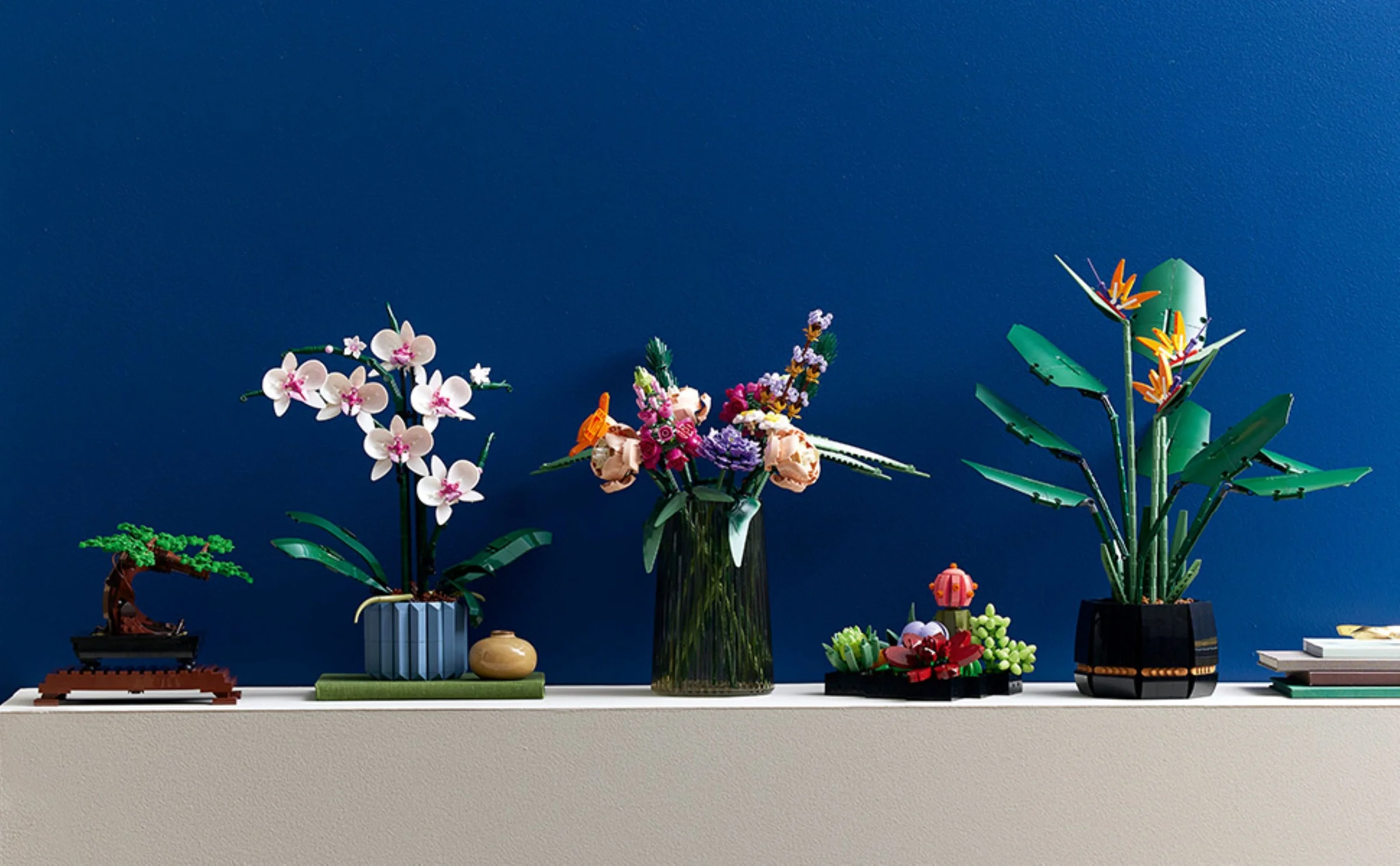 O vedere cu mai multe seturi LEGO Botanical Collection pe un raft alb, fundal albastru. O orhidee, un buchet și o pasăre a paradisului.