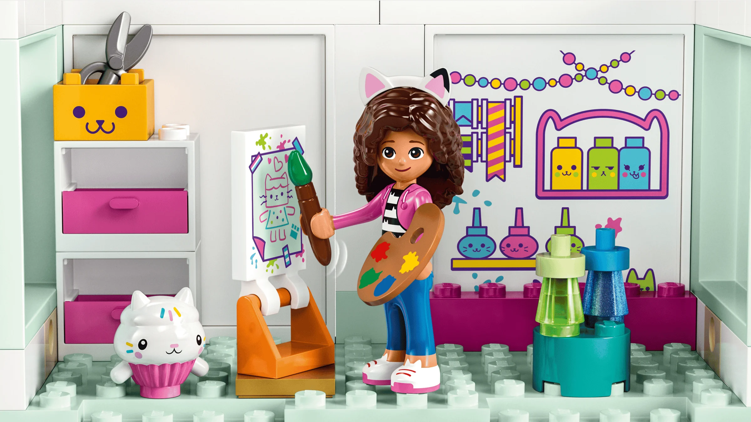 Gabby pictează cu pensula și paleta într-un atelier colorat din setul LEGO Gabby's Dollhouse.