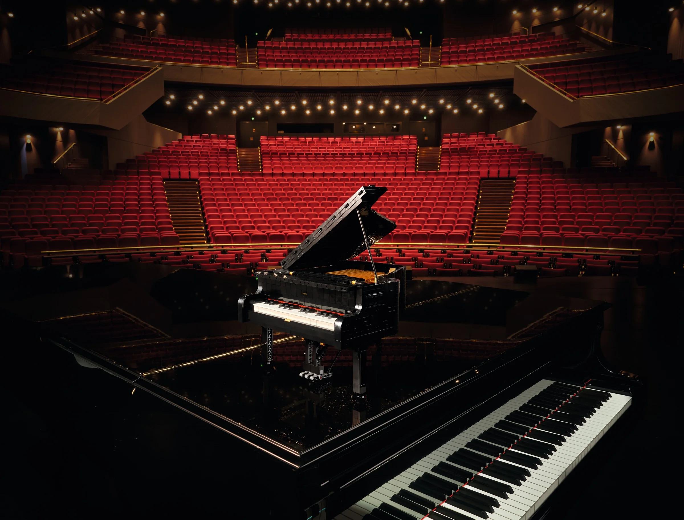 Pianul LEGO stă pe scenă, într-o sală de concert goală, cu scaune roșii.