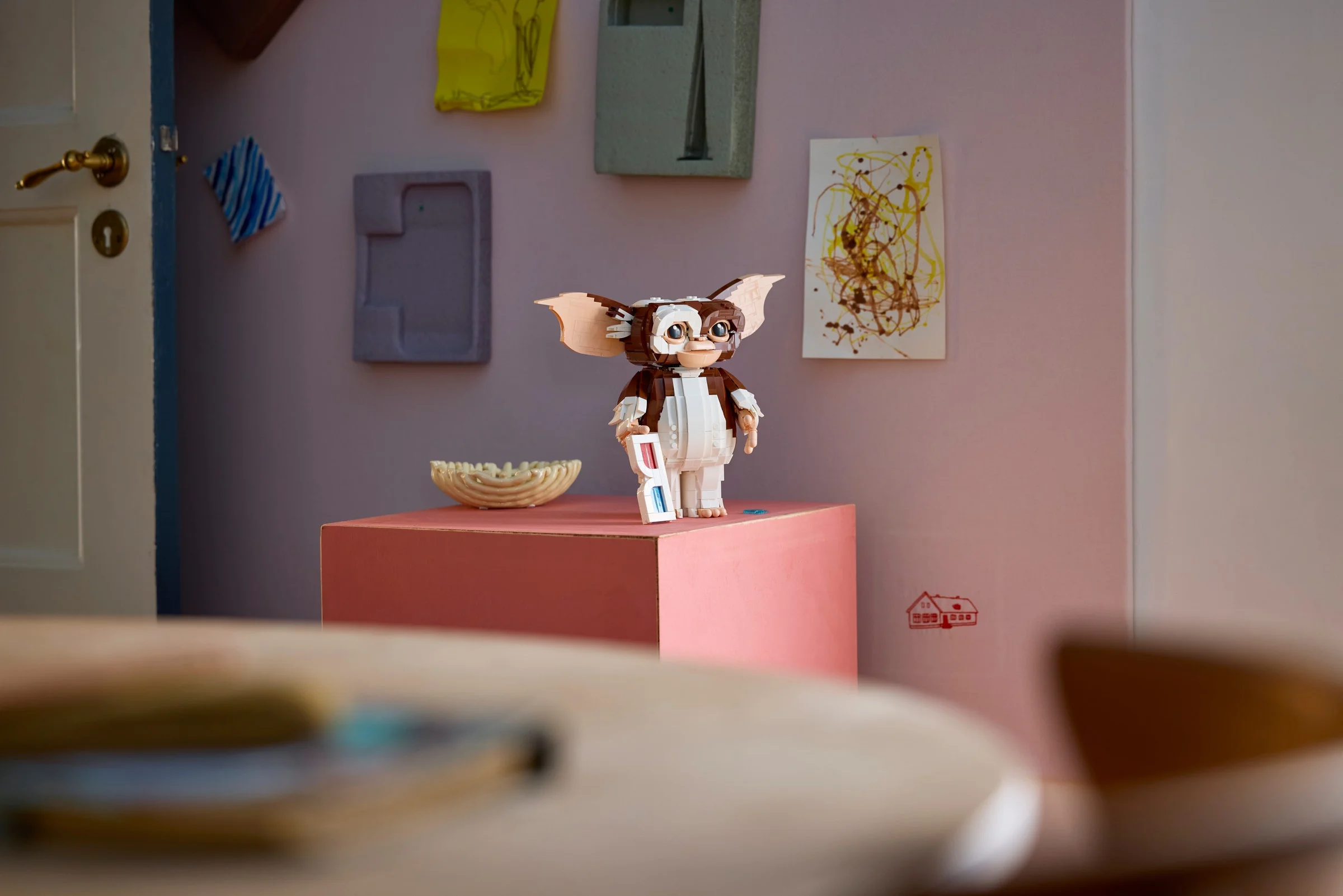 Gizmo LEGO stând cu ochelari 3D, într-o cameră decorată artistic.