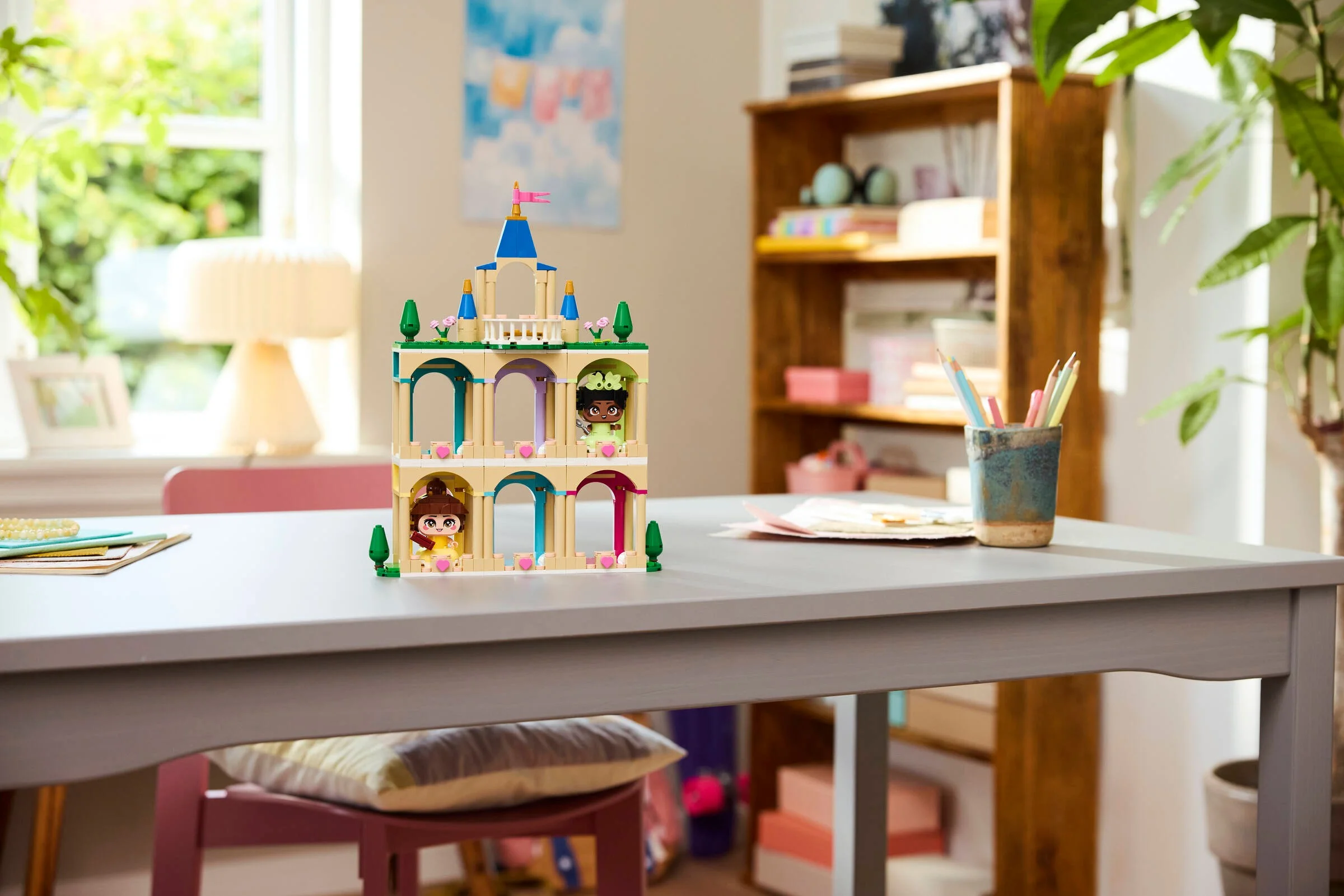 Castelul mini LEGO cu Belle și Tiana expus pe o masă într-o cameră luminoasă.