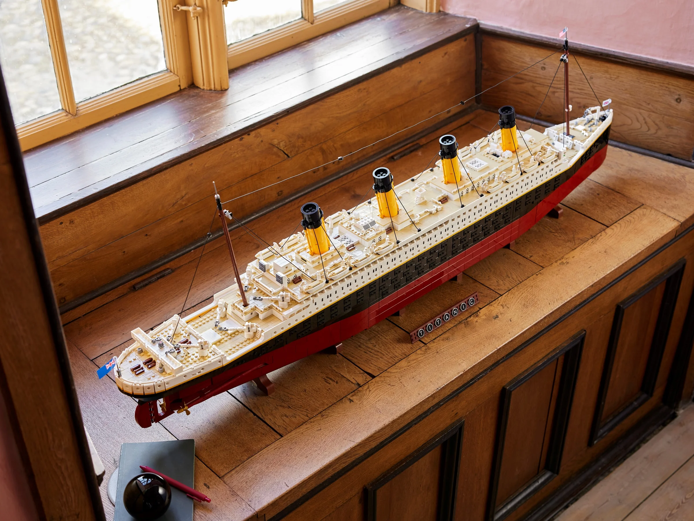 Modelul LEGO Titanic, expus pe o suprafață de lemn lustruită lângă o fereastră luminoasă.