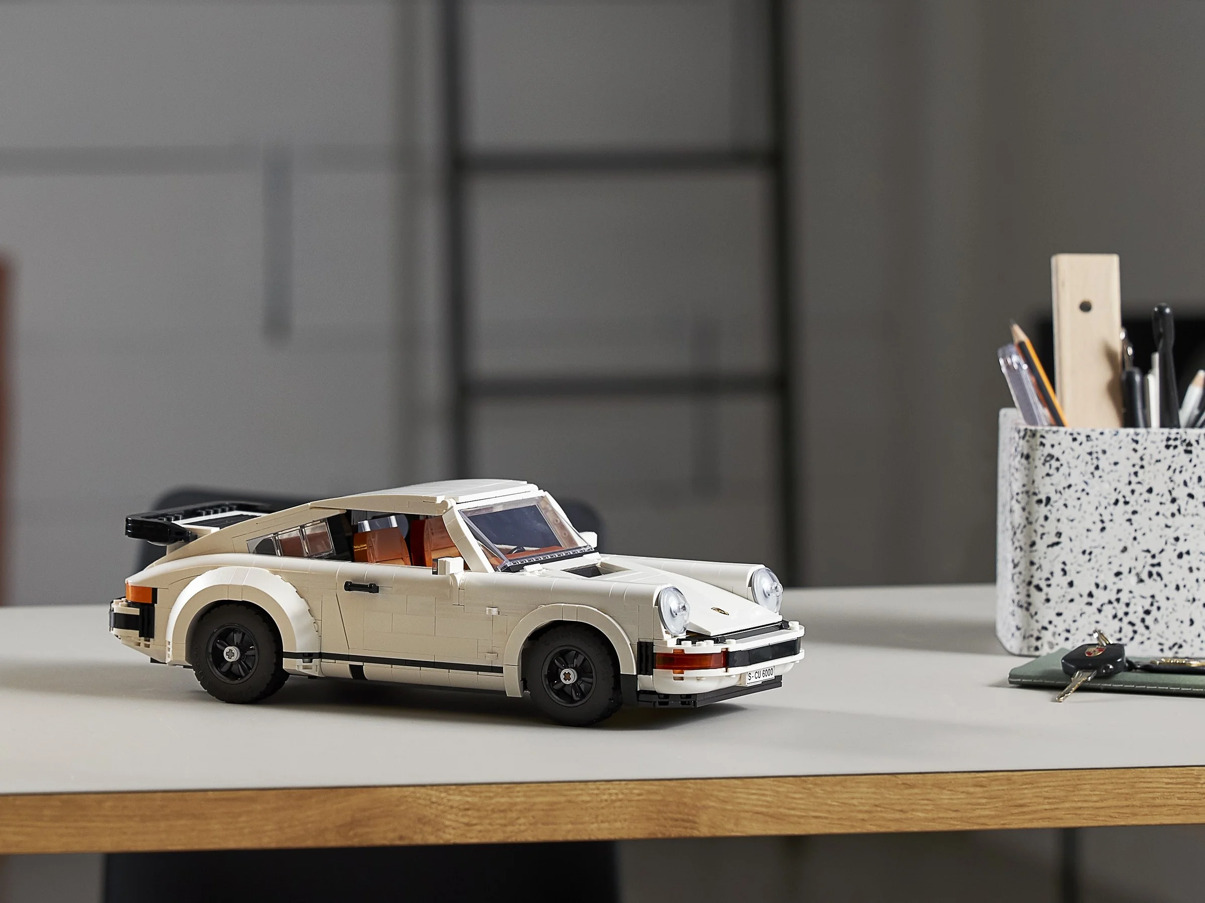 Imagine cu modelul LEGO Porsche 911, alb, aranjat pe o masă într-un birou modern.