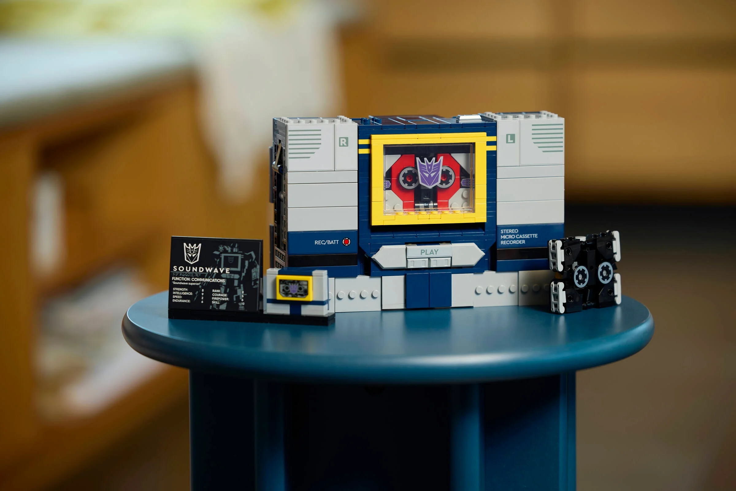 Imagine cu modelul LEGO Soundwave, carte și casetă, pe un suport albastru.