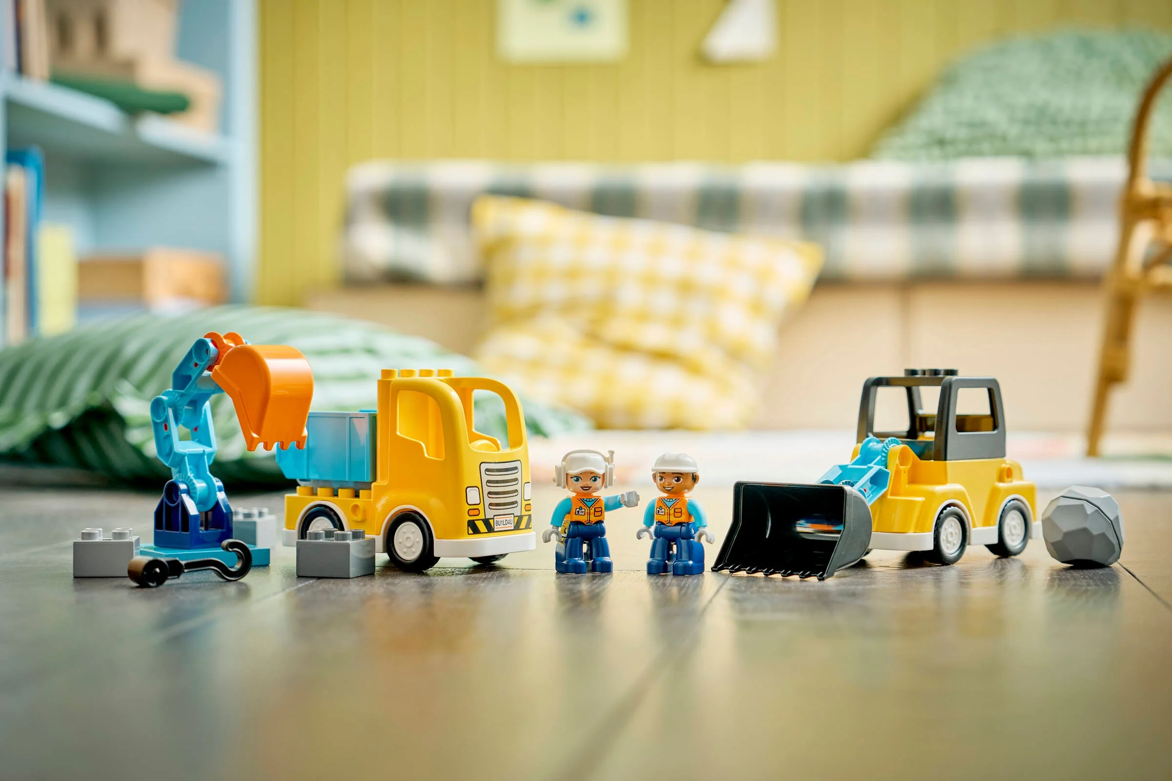 Imagine cu cele 3 vehicule de construcție Duplo și 2 figurine, pe o suprafață de lemn.