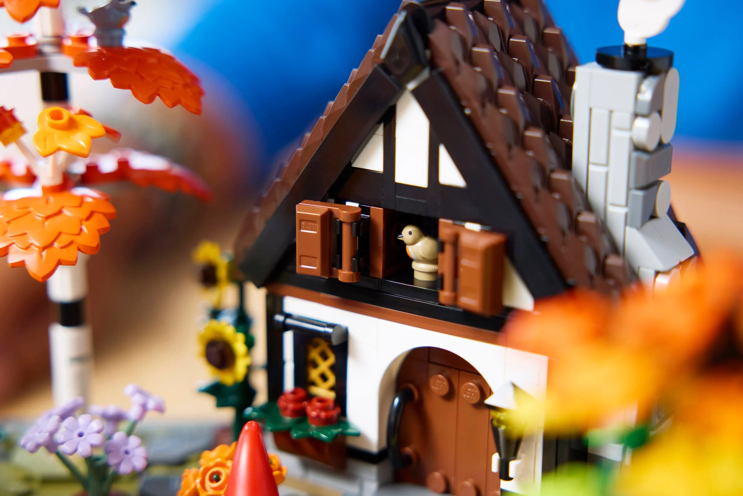Cadrul prezintă o casă de țară LEGO cu detalii de toamnă: acoperiș maro, flori și un coș de fum.