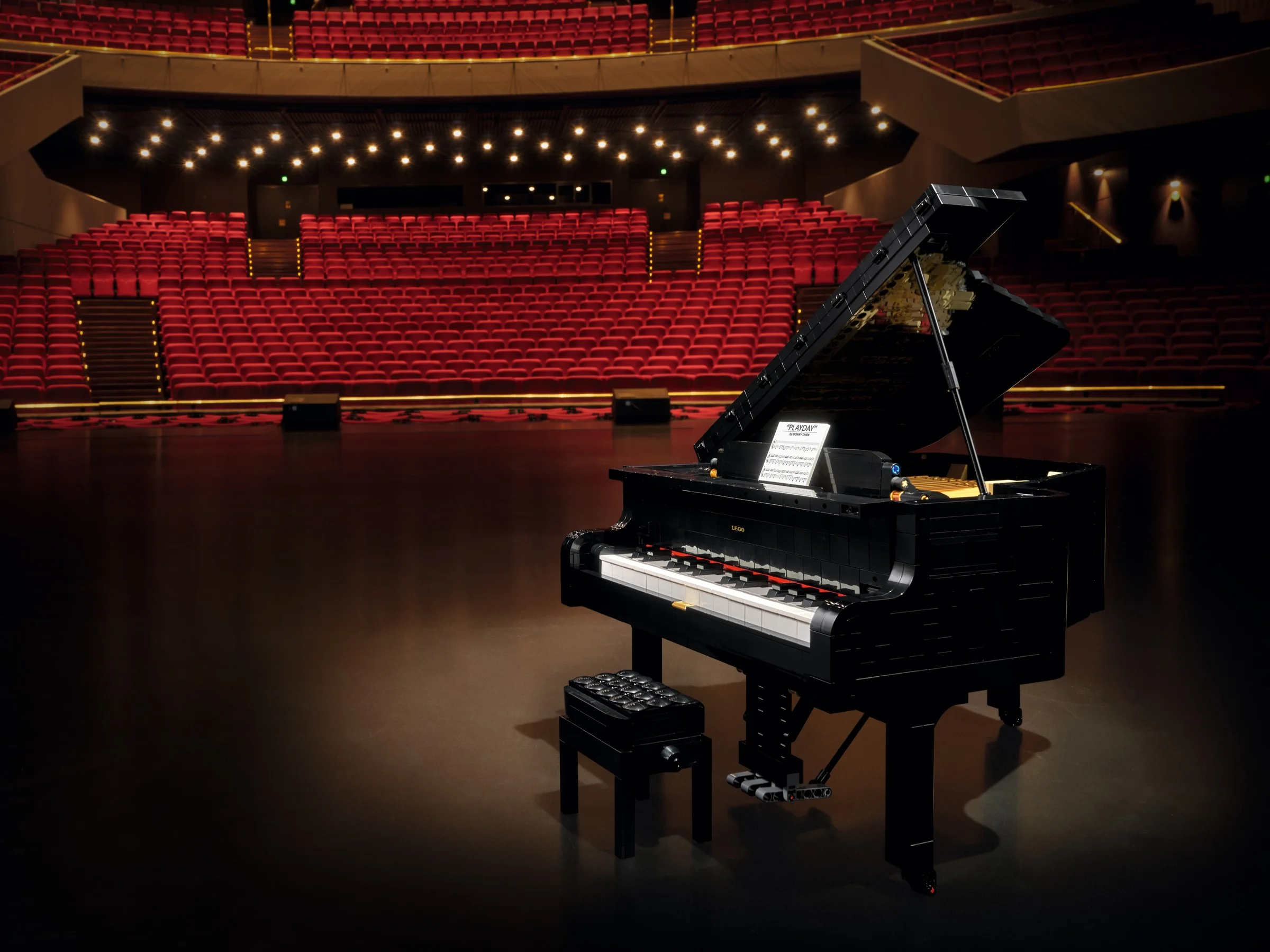 Pianul LEGO Grand Piano 21323, amplasat pe o scenă, cu scaun și partitură.
