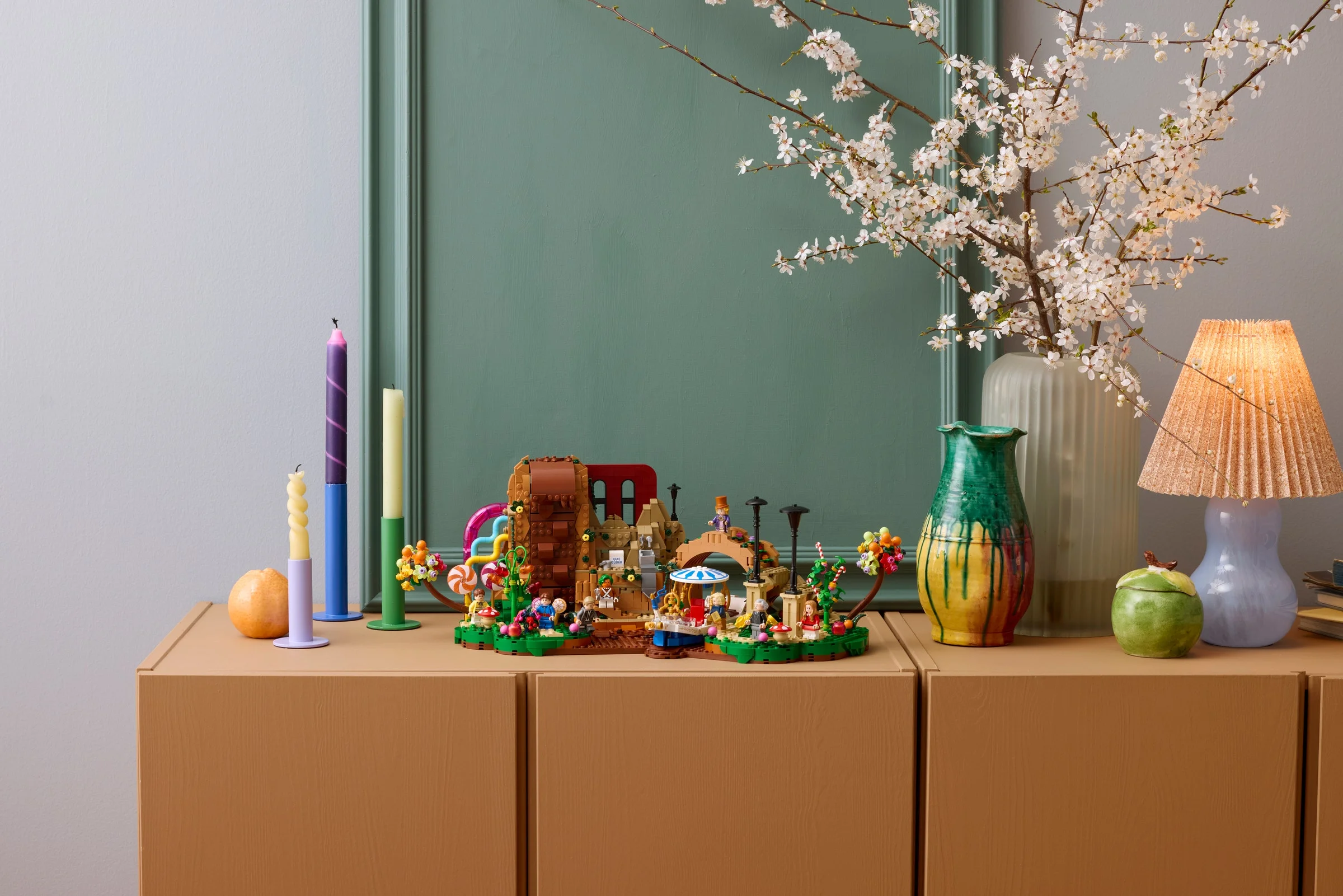 Modelul LEGO Willy Wonka, decorat pe o comodă maro, arată fabrica de ciocolată și minifigurine.