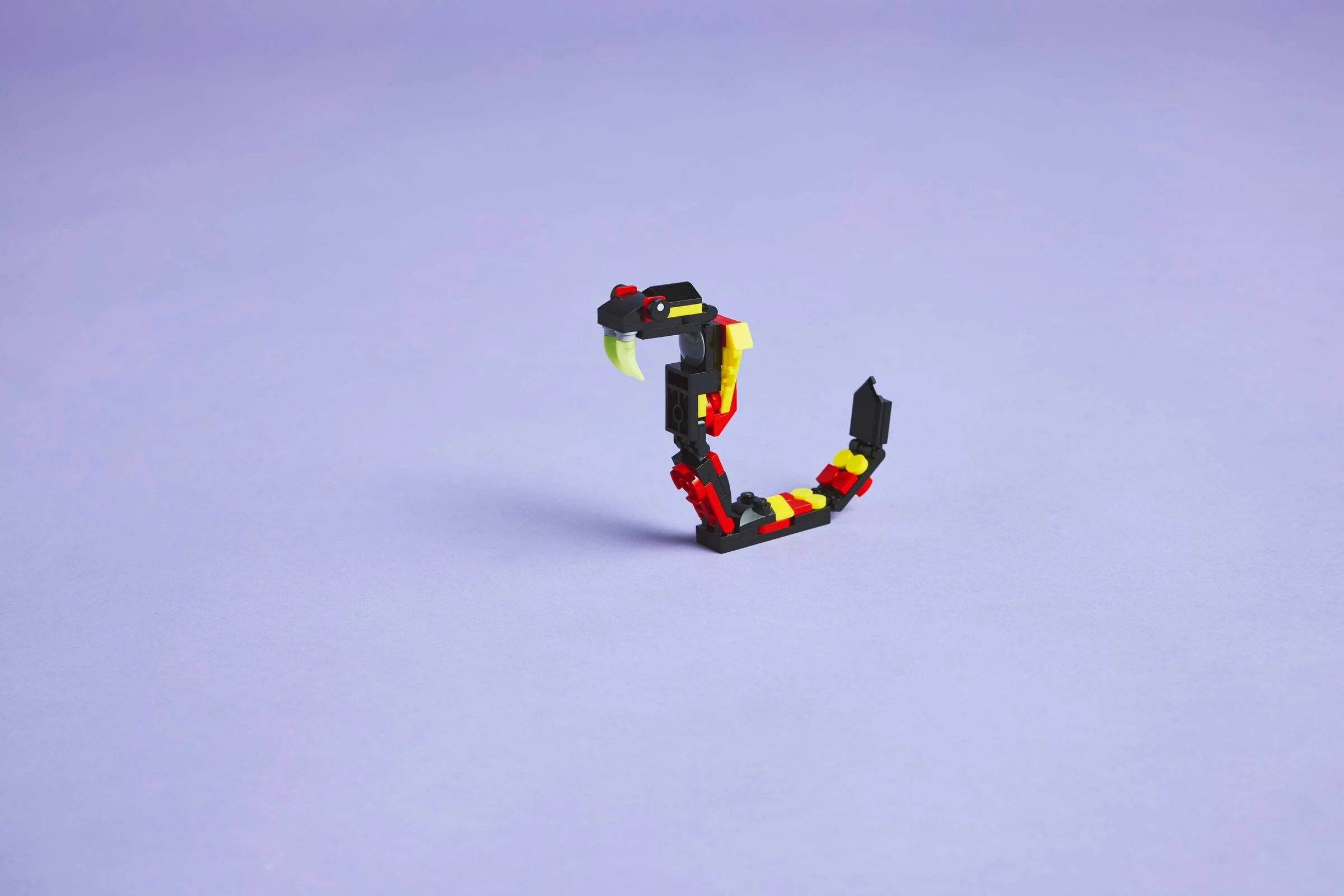 Modelul LEGO Creator 31159, șarpe cu colți, negru, roșu și galben pe fundal violet.