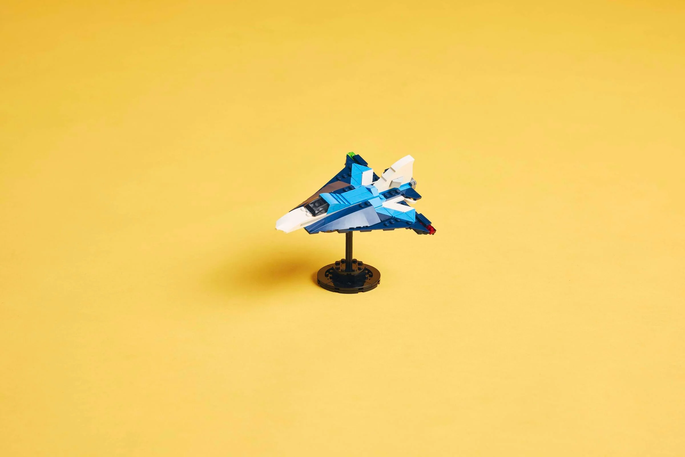 Avion de curse albastru și alb din LEGO pe un stativ negru, fundal galben.