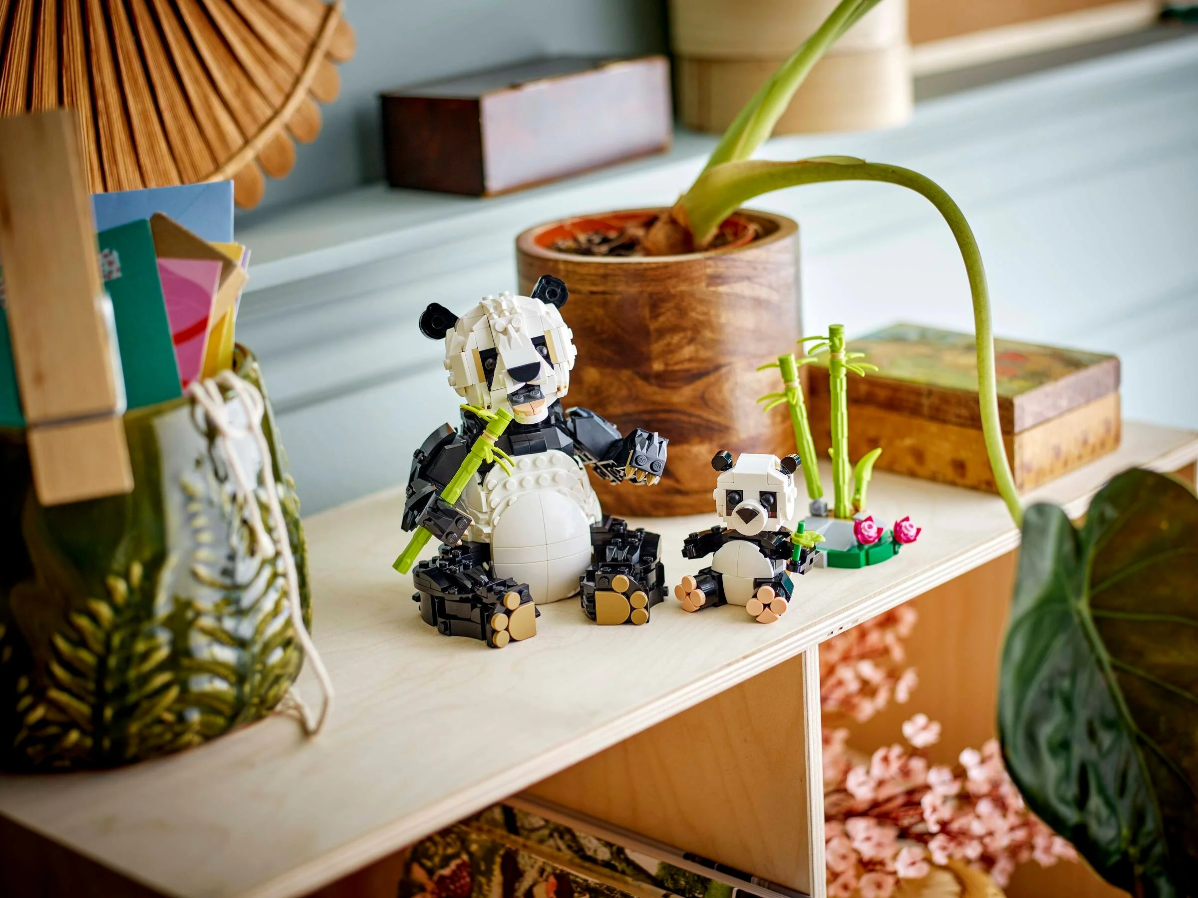 O familie drăguță de panda construite din LEGO, inclusiv bambus, prezentată pe o etajeră.