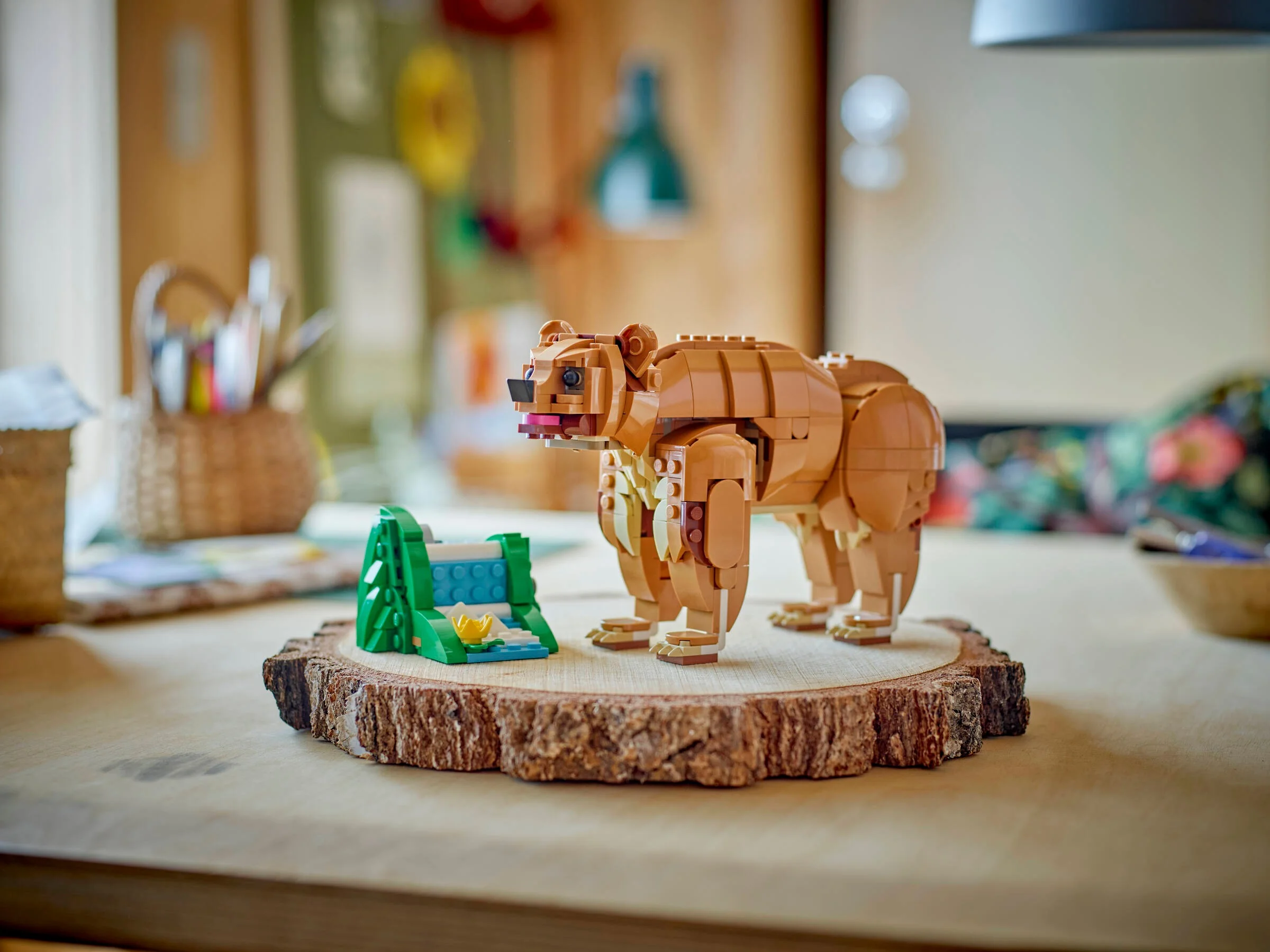 Imagine cu un urs LEGO maro și o cascadă mică, pe o felie de lemn. Fundal estompat.