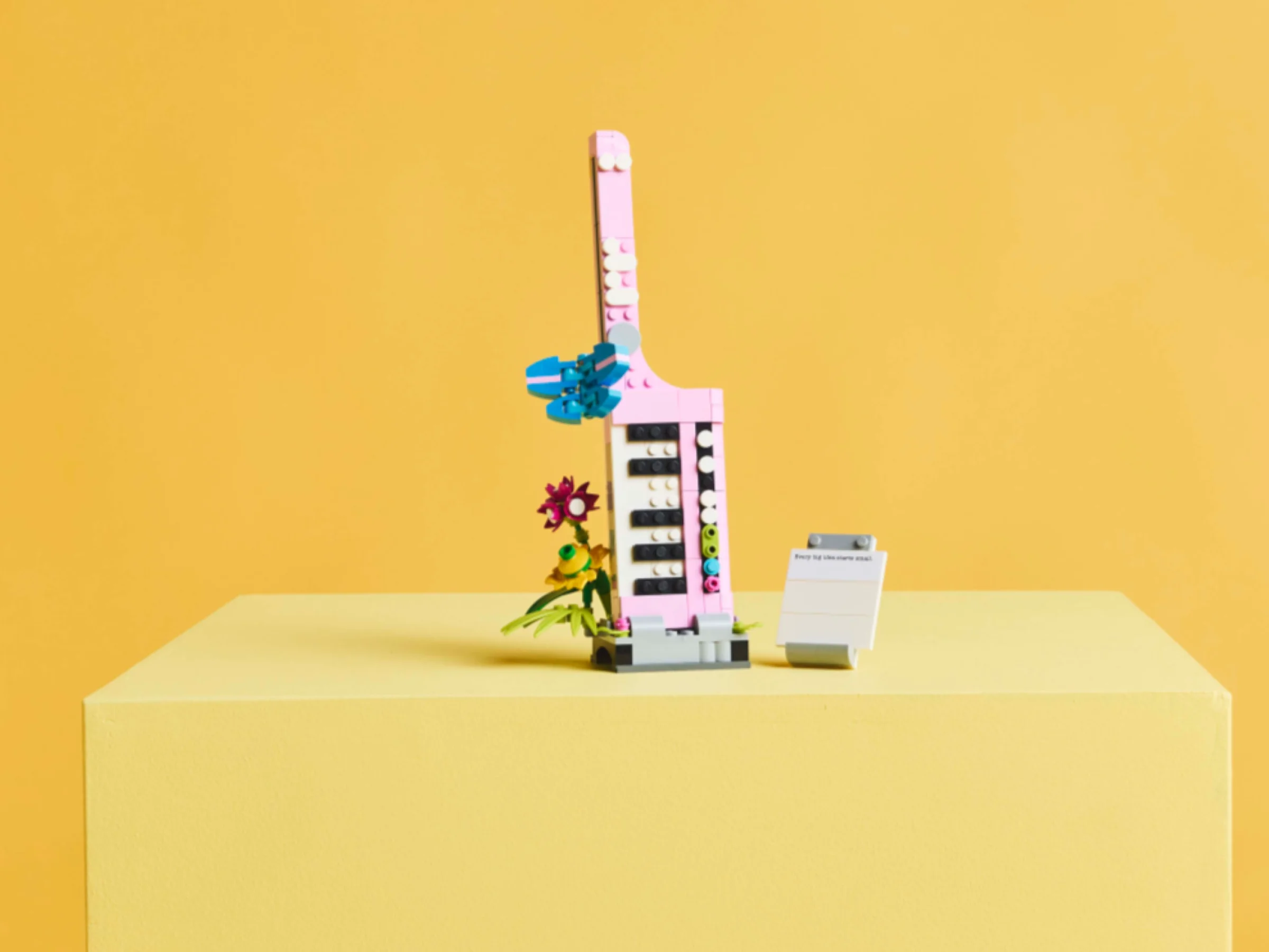 Modelul LEGO de mașină de scris roz cu flori, pe un fundal galben.