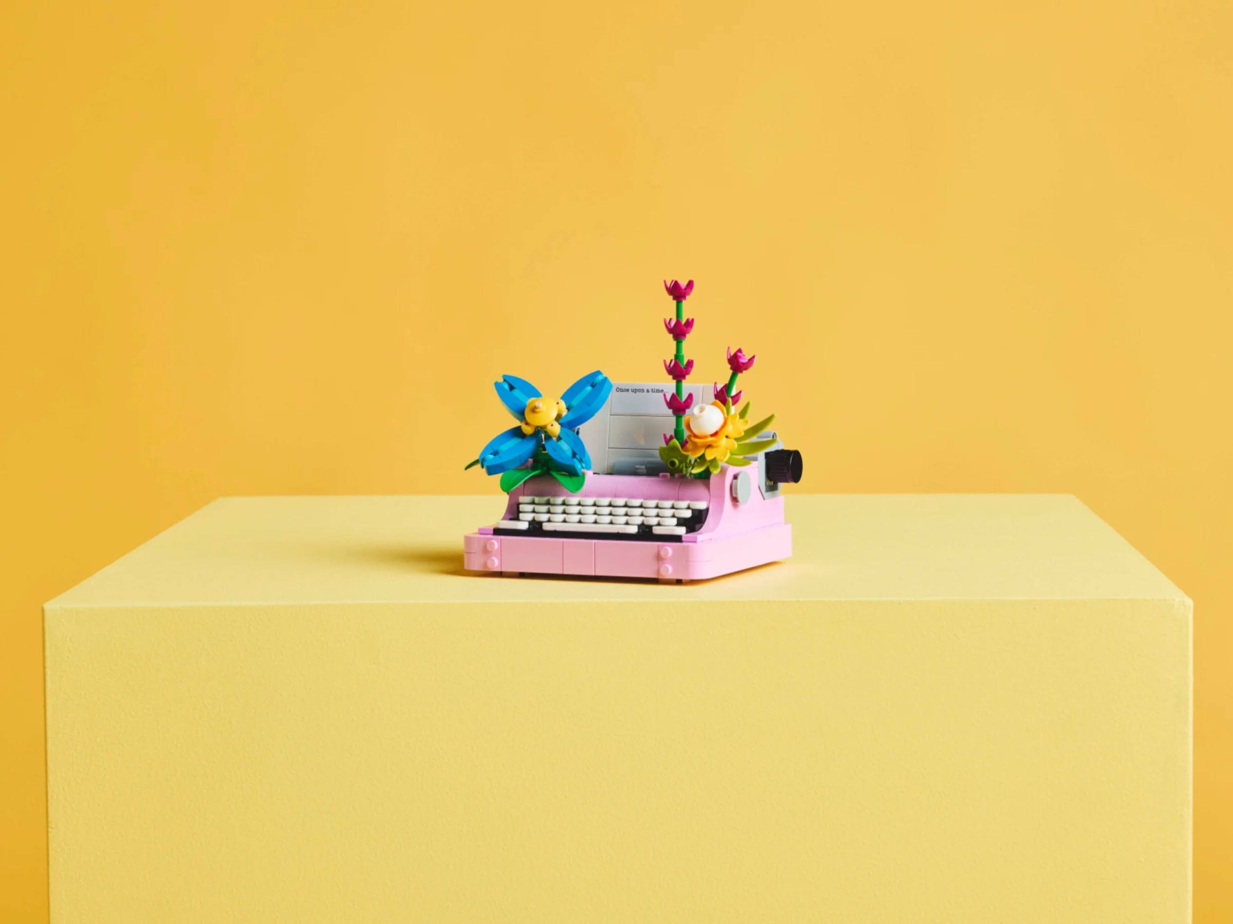 O imagine statică a modelului LEGO, o mașină de scris roz, cu flori colorate deasupra.