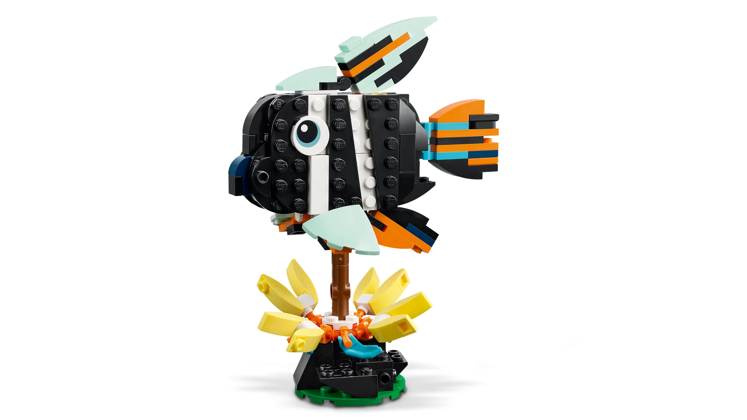 Model LEGO al unui pește tropical colorat, pe o bază cu flori galbene.