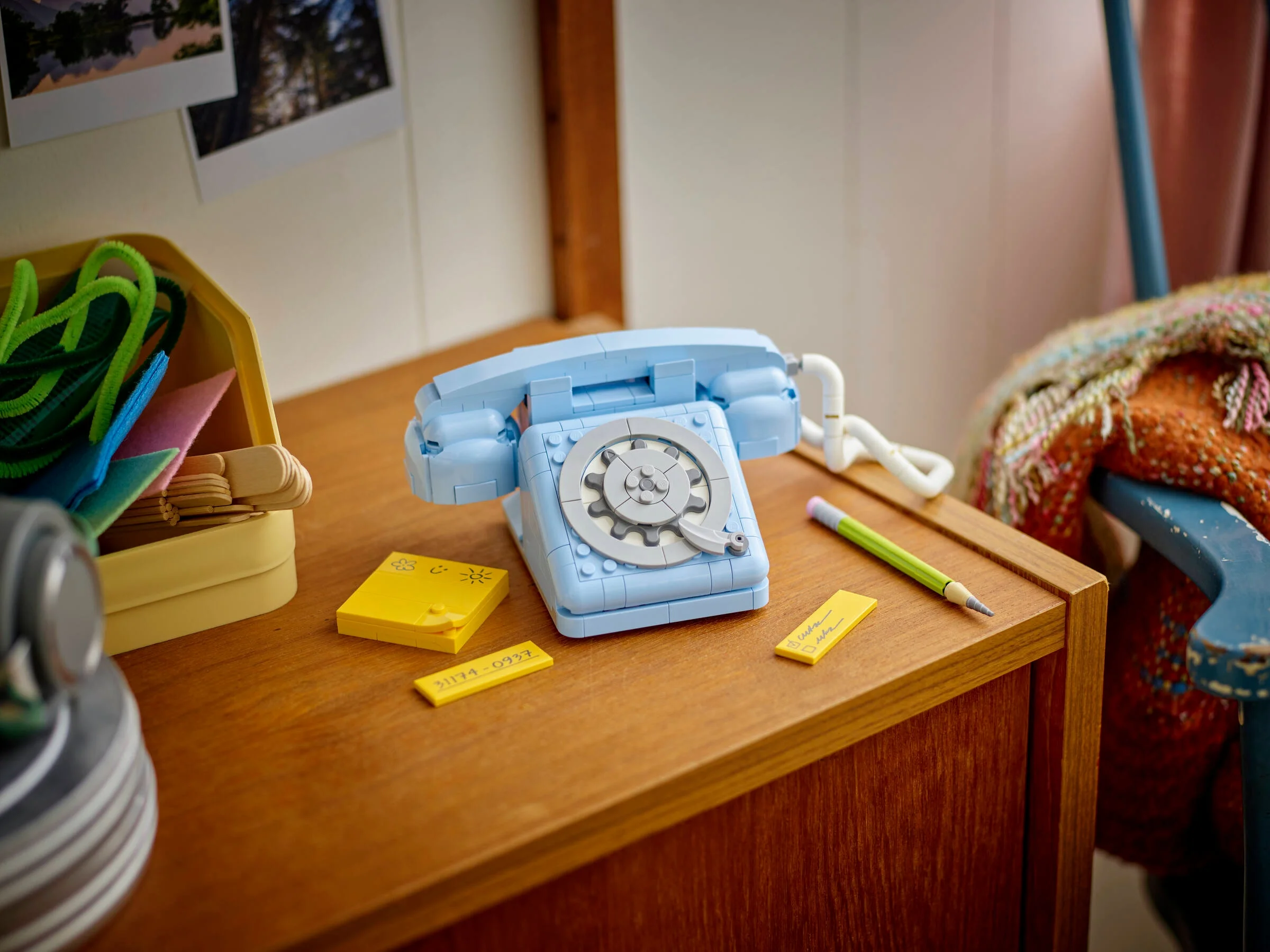Telefonul retro LEGO albastru stă pe un birou cu post-it-uri și un creion.