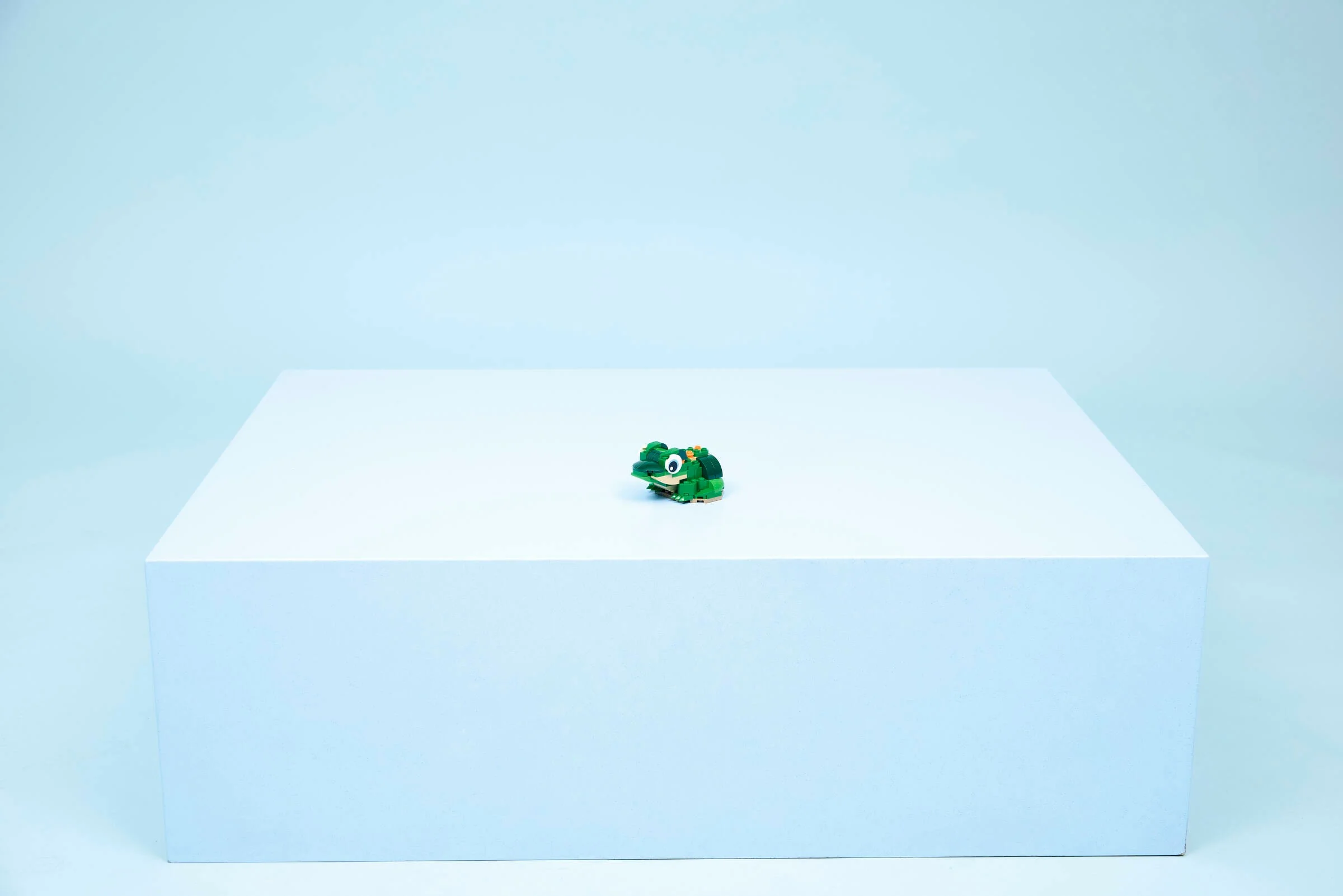 O broască țestoasă verde din LEGO pe un cub alb, fundal albastru deschis.