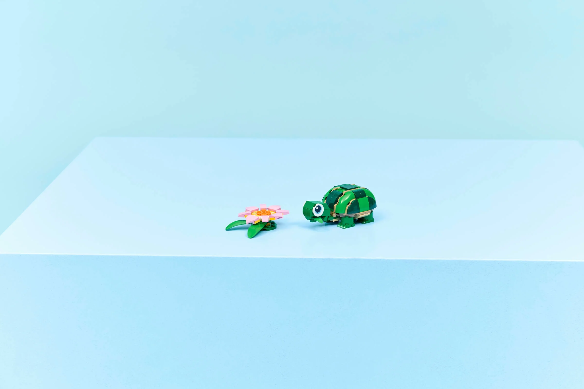 O broască țestoasă LEGO verde cu un nufăr roz pe un fundal albastru. Model finalizat.